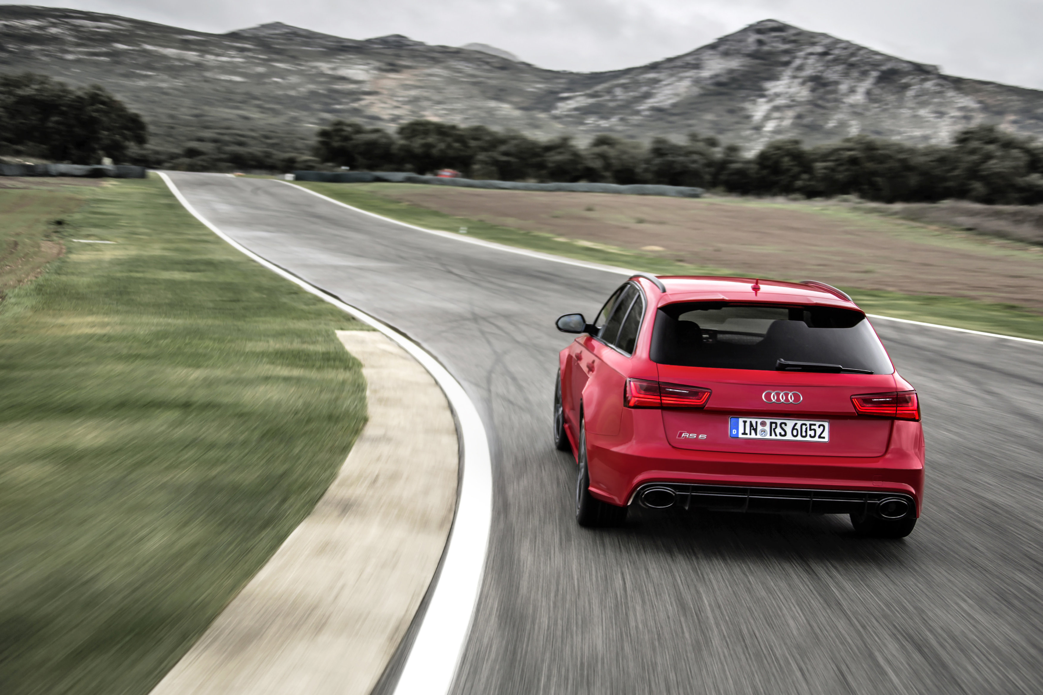 Roter Audi RS fährt auf kurvenreicher Rennstrecke, umgeben von grünen Wiesen und bewaldeten Hügeln im Hintergrund.