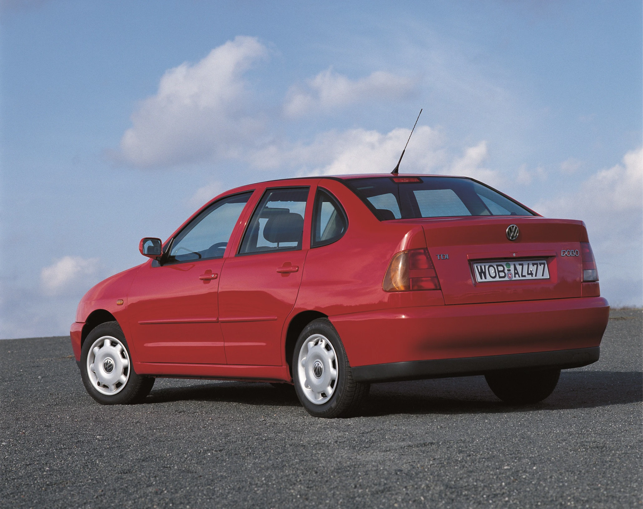Rotes Auto, Modell VW Polo Classic, auf einer Asphaltfläche vor blauem Himmel mit Wolken. Rückansicht, kompakte Limousine.