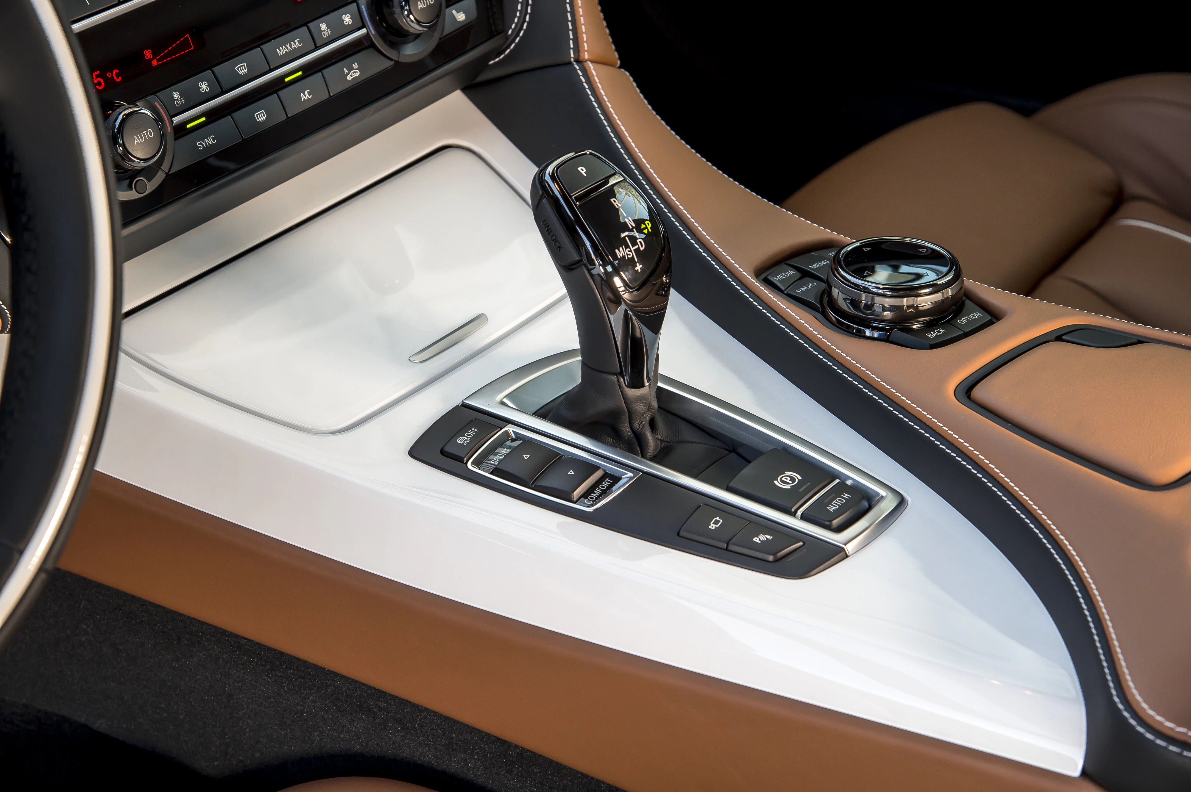 Nahaufnahme einer modernen Automittelkonsole mit Automatikschalthebel, braunem und weißem Interieur sowie einem Drehknopf für Bedienelemente.
