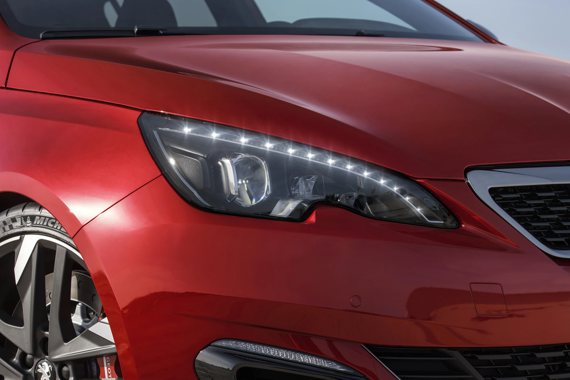 Rotes Auto mit modernen Frontscheinwerfern und stylischen Felgen, Frontalansicht auf das Scheinwerfer- und Karosseriedetail.