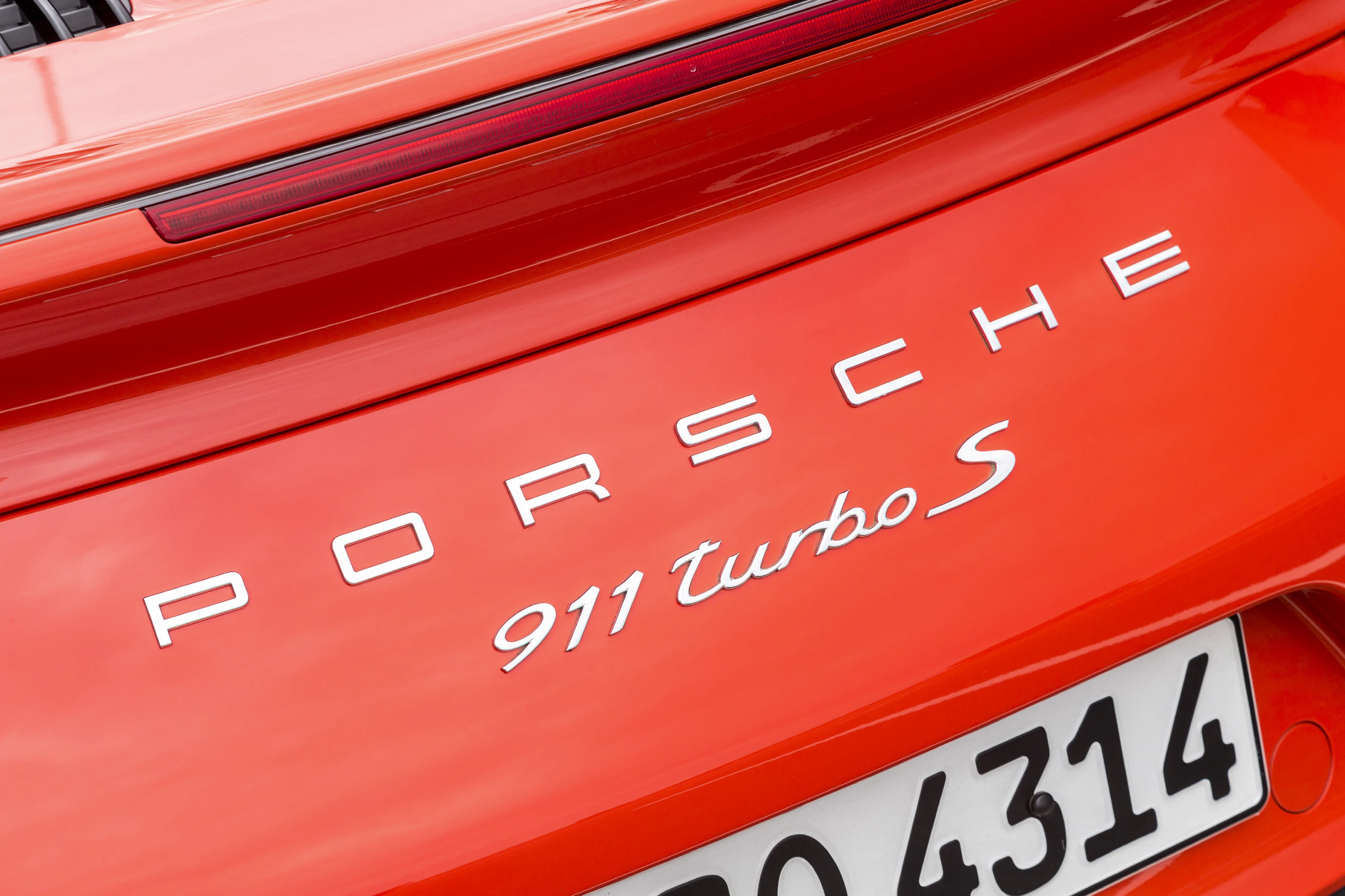 Roter Porsche 911 Turbo S, Nahaufnahme des Emblems auf dem Heck mit sichtbarem Kennzeichen.