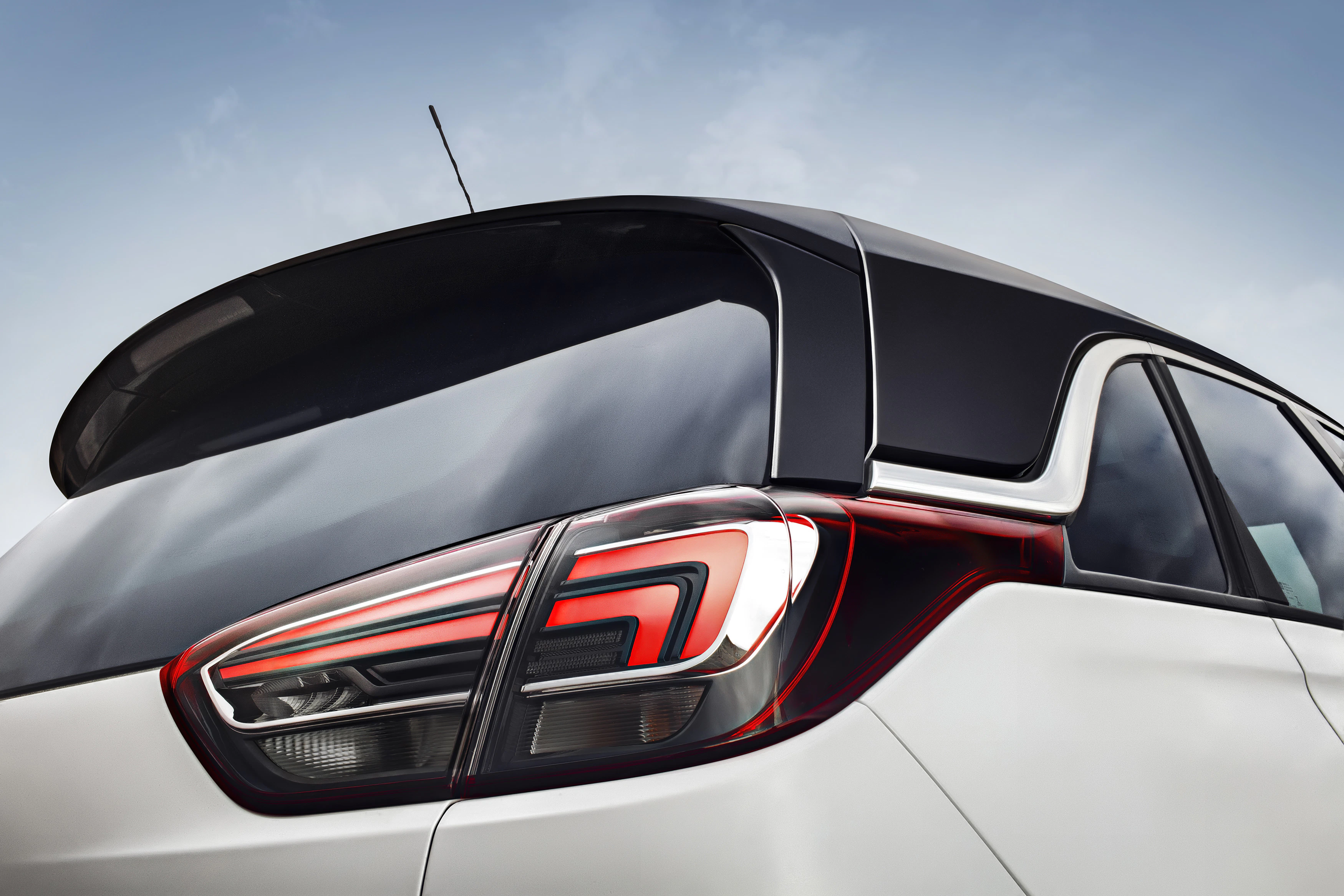 Rückansicht eines modernen Autos mit markanten, aerodynamischen Linien und einem auffälligen, rot-schwarzen Rücklicht unter klarem Himmel.
