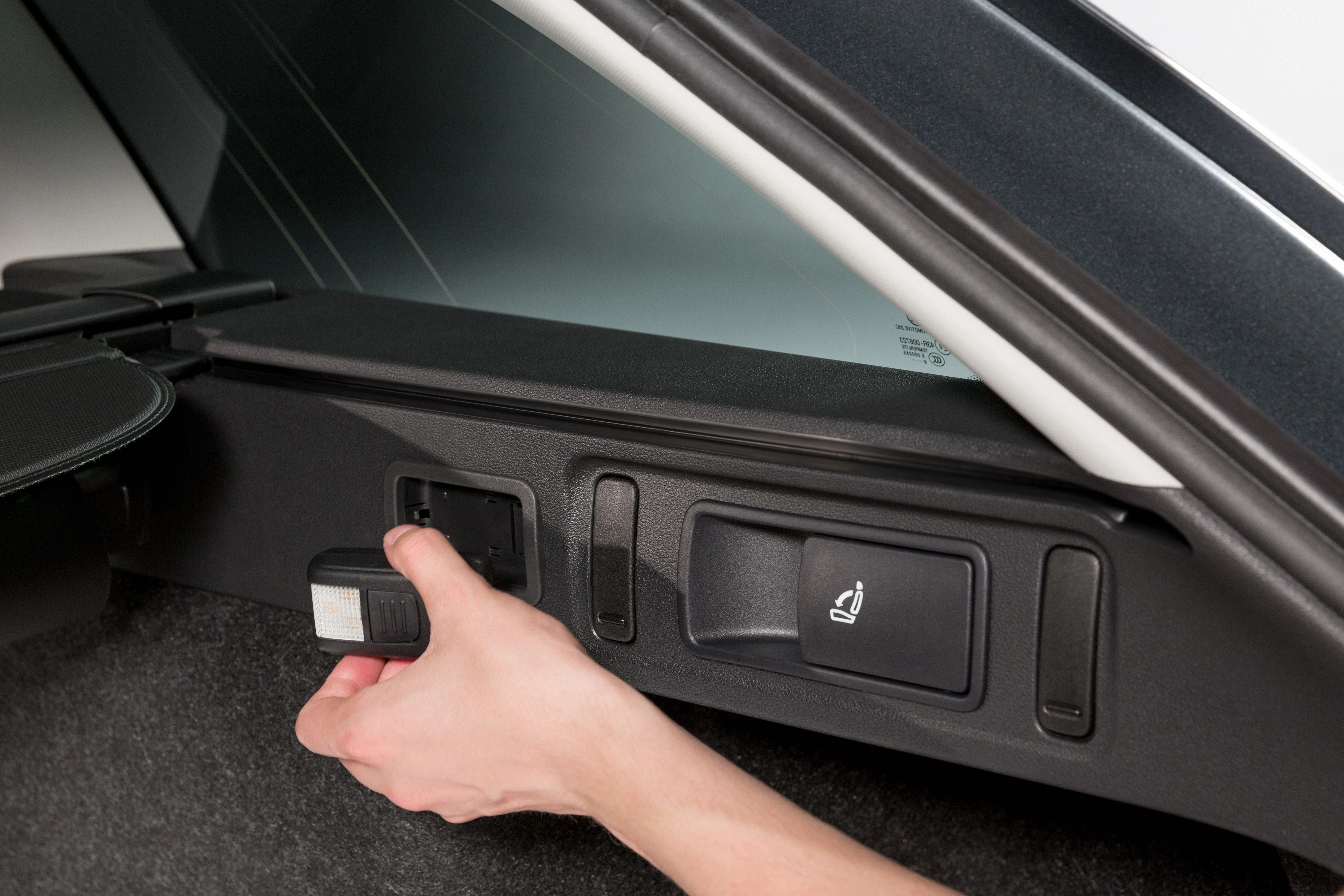 Person bedient Hebel im Kofferraum eines Autos zur Rücksitzentriegelung. Klar erkennbar ist das Sitzsymbol auf dem Hebel.