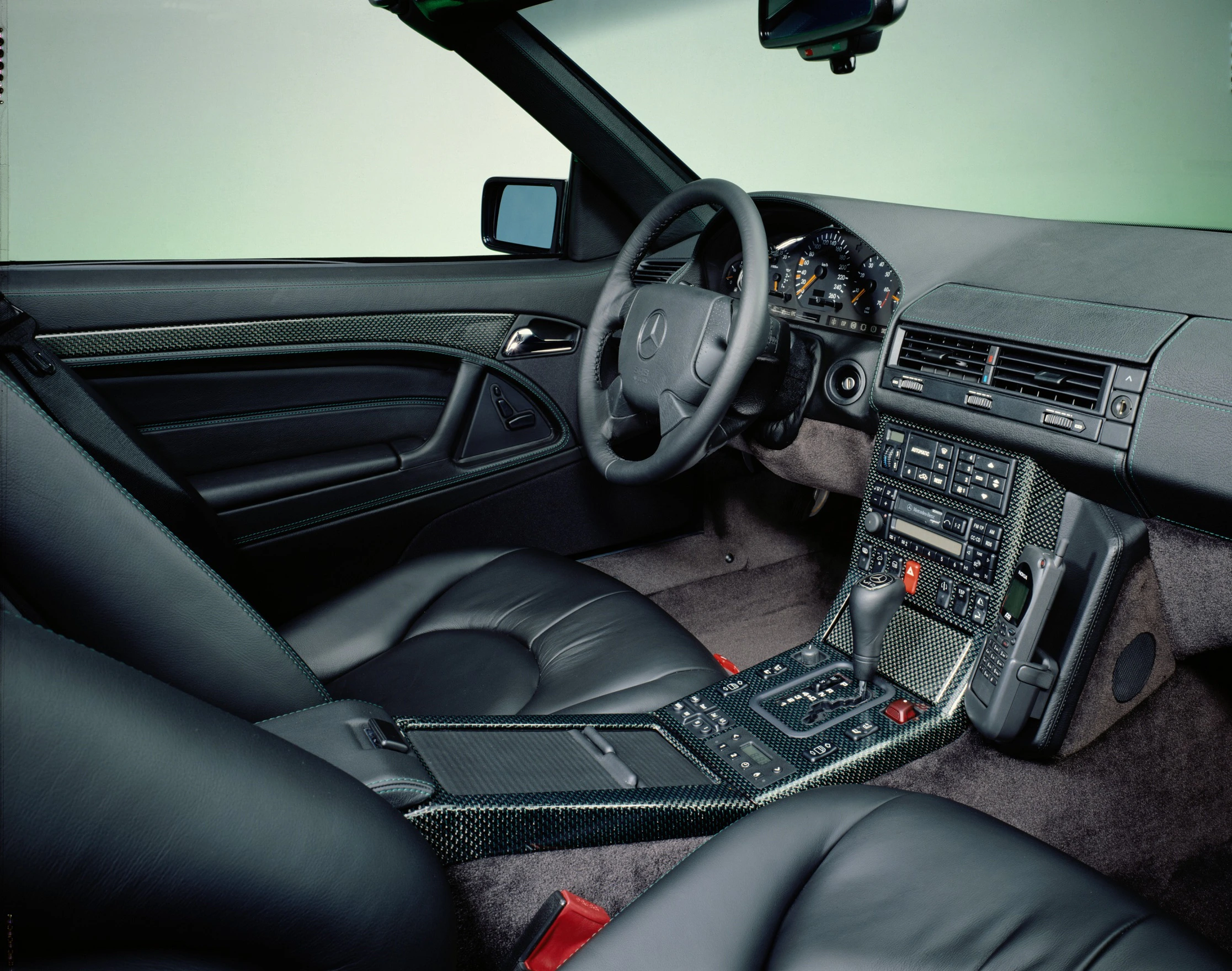 Innenraum eines Mercedes mit schwarzer Lederausstattung, Karbonverkleidung und klassischem Armaturenbrettdesign.