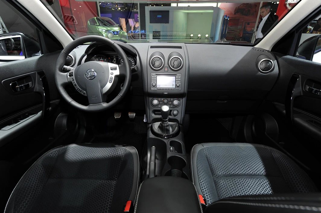 Innenraum eines Autos mit schwarzer Polsterung und moderner Instrumententafel. Lenkrad links, Handbremse und Schalthebel in der Mitte.