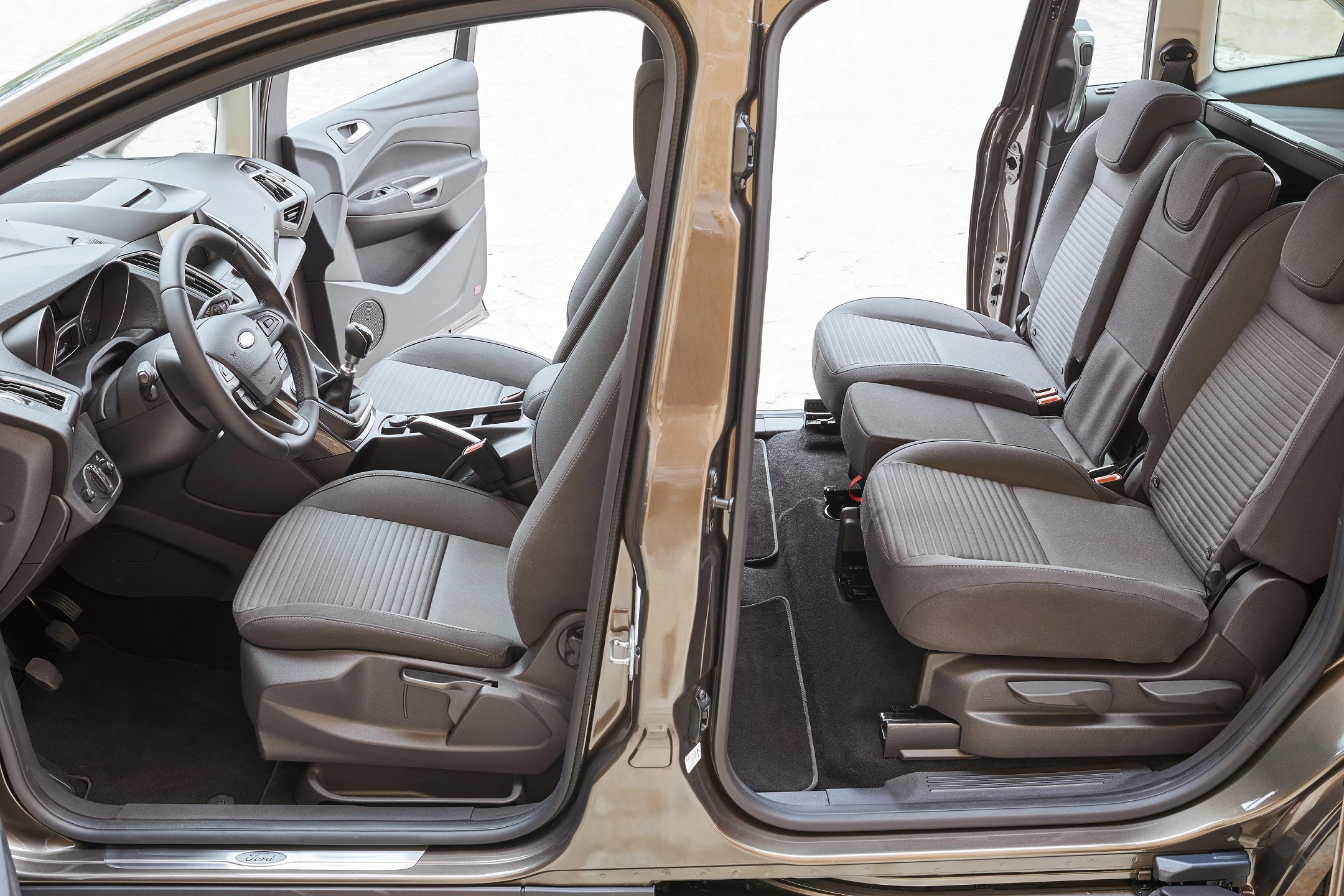 Innenansicht eines Autos mit geöffneter Tür, zwei Reihen von Sitzen sichtbar, graue Polsterung, geräumiger Innenraum.