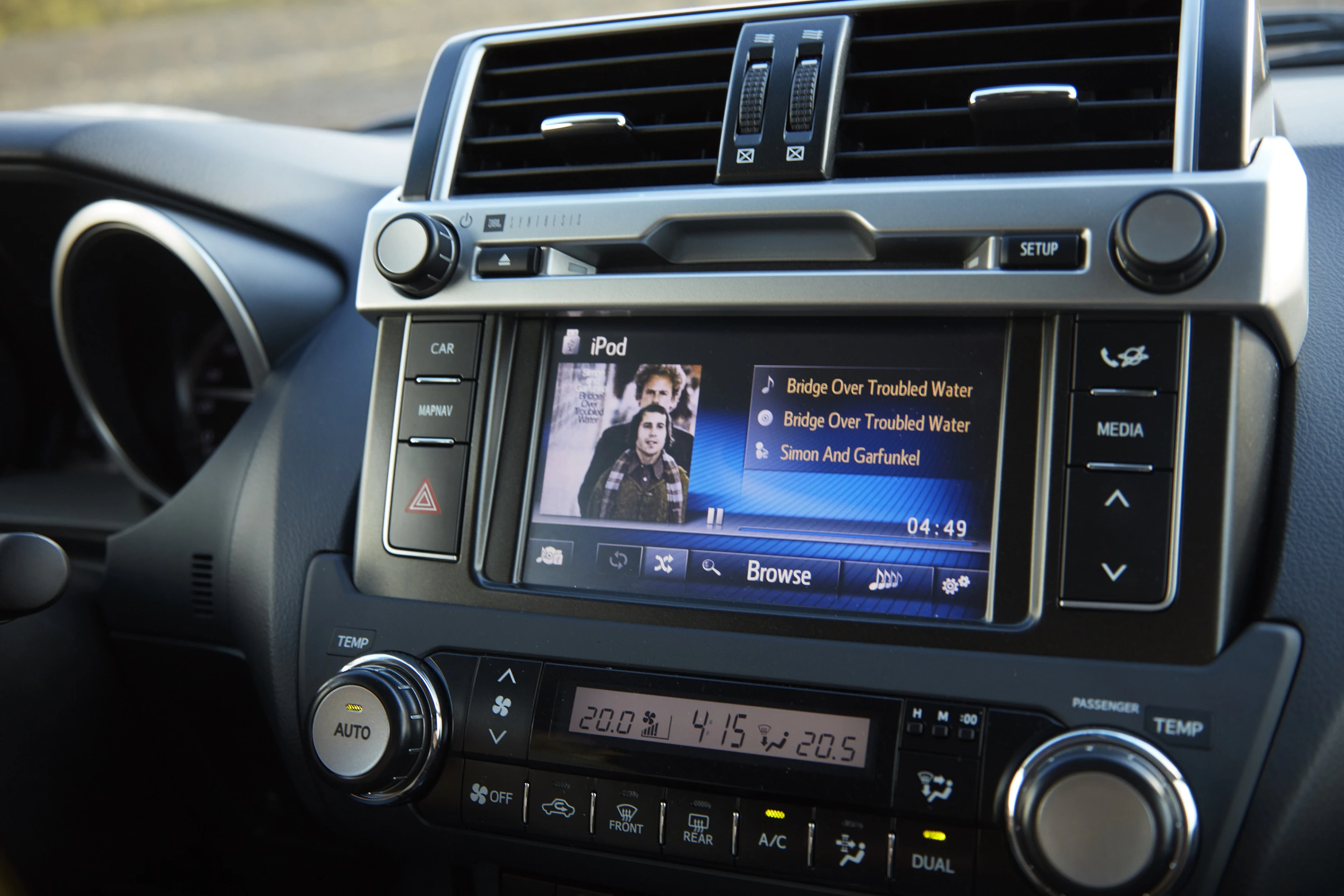 Autoradio zeigt "Bridge Over Troubled Water" von Simon and Garfunkel auf einem iPod-Interface. Klimaanlagensteuerung unten sichtbar.