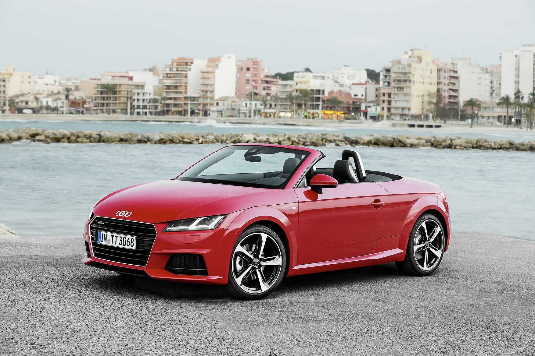 Roter Audi TT Cabrio geparkt vor städtischer Küstenkulisse mit mehrstöckigen Gebäuden im Hintergrund.