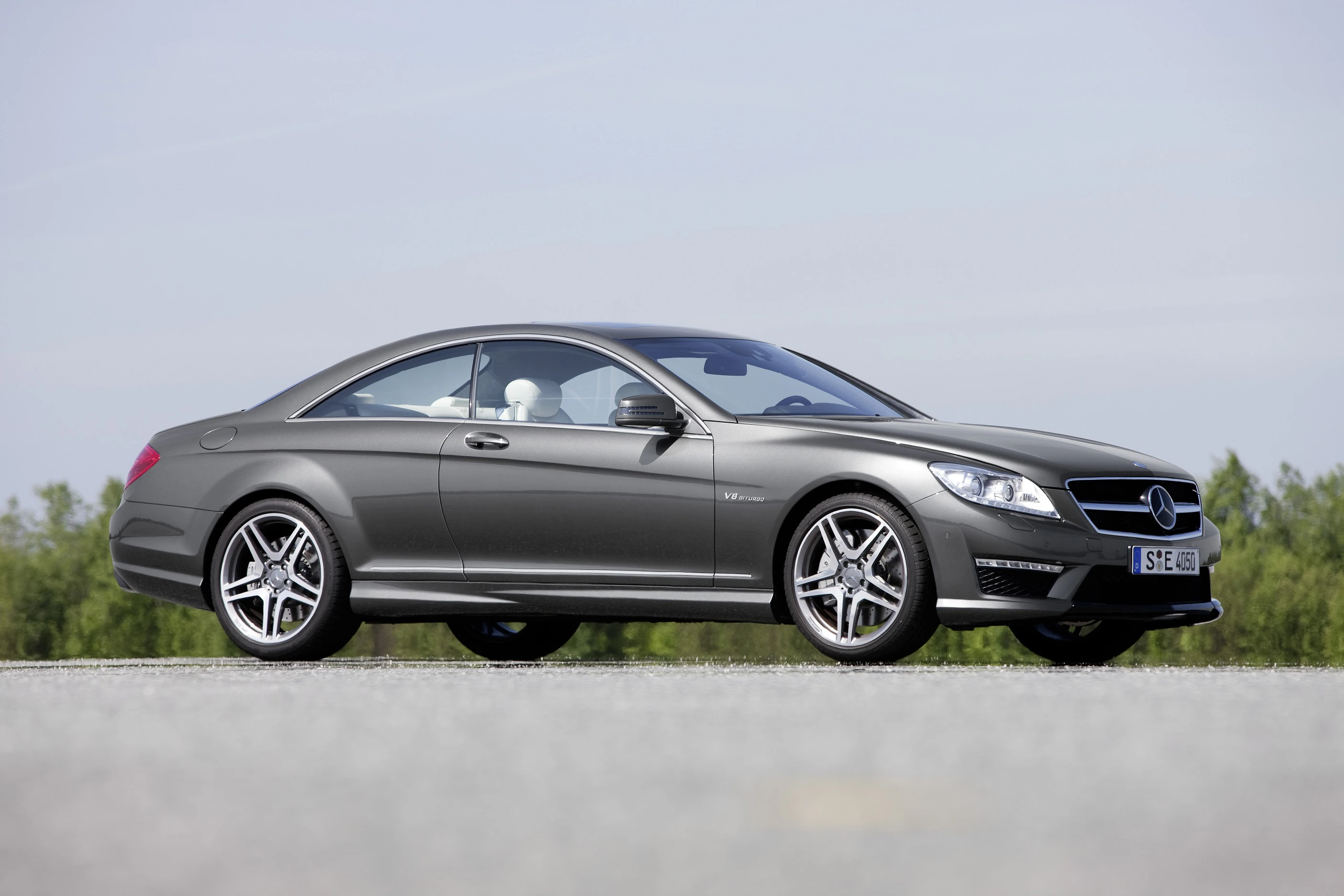 Graues Mercedes-Benz Coupé, seitliche Ansicht, auf einer Straße vor bewölktem Himmel. Elegantes Design, sportliche Karosserie.