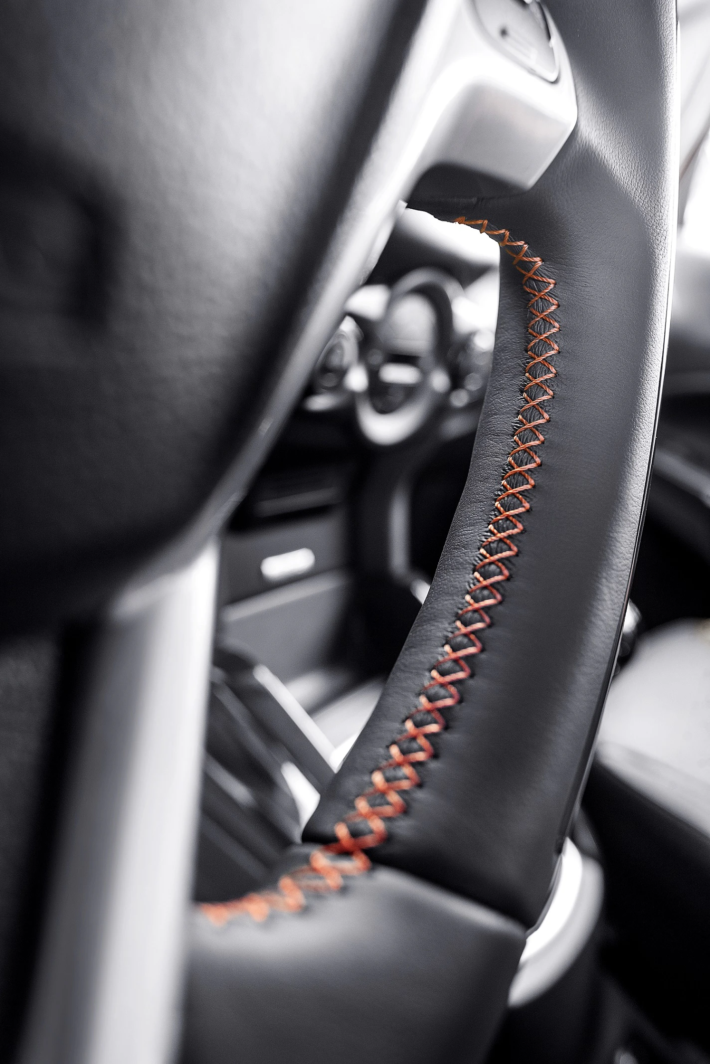 Nahaufnahme eines Lenkrads mit rotbrauner Naht in einem modernen Auto. Im Hintergrund ist unscharf der Innenraum sichtbar.
