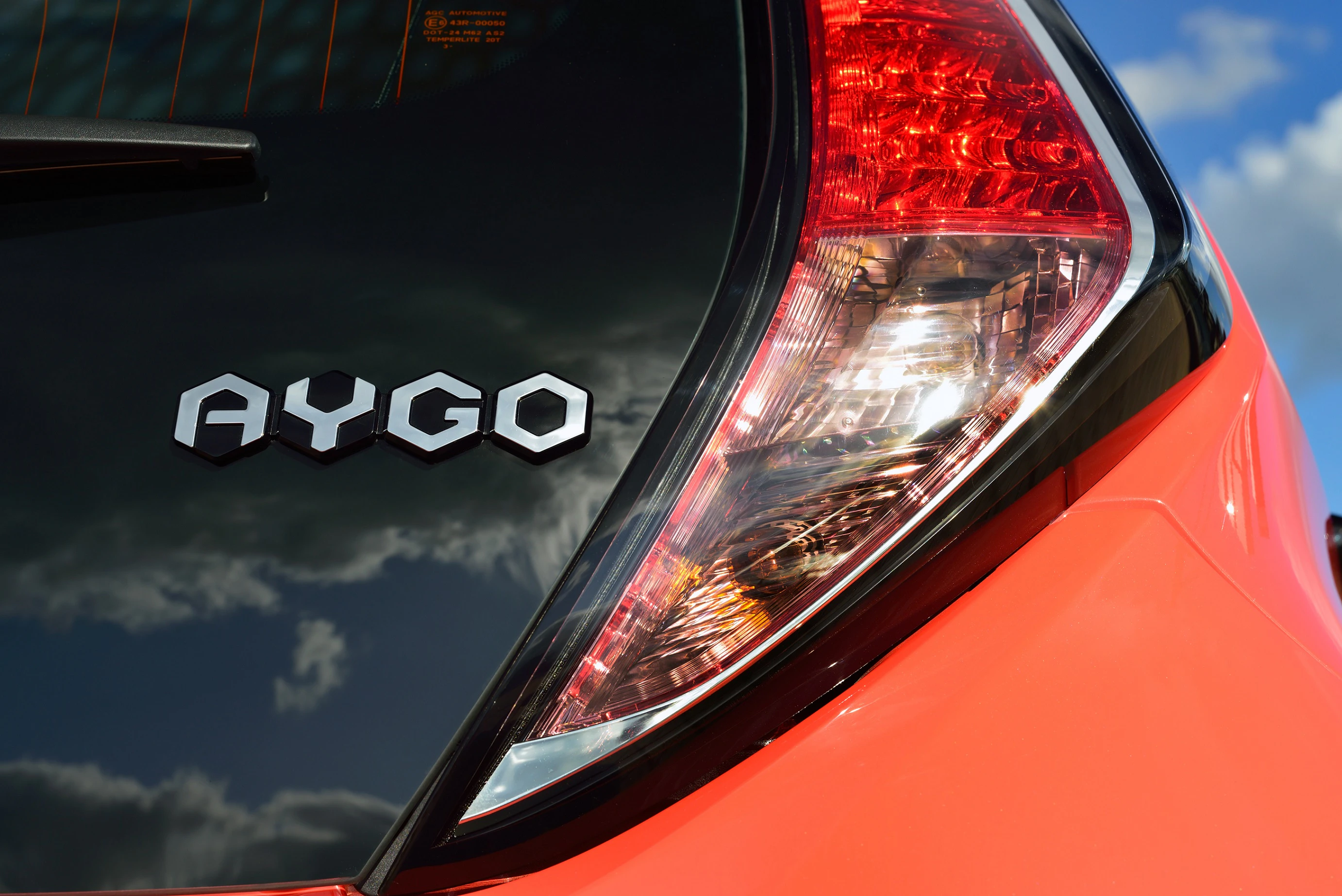 Rückansicht eines orangefarbenen Autos mit dem Schriftzug „AYGO“ und einem modern designten Rücklicht unter blauem Himmel.
