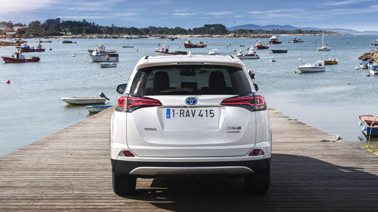 Weißer SUV auf einem Holzsteg mit Meer und vielen Booten im Hintergrund unter blauem Himmel.