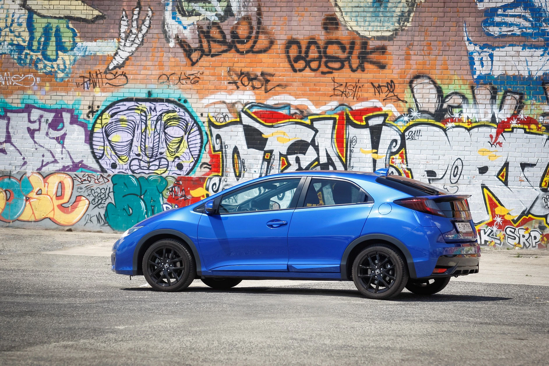 Blauer Sportwagen steht vor einer mit buntem Graffiti besprühten Wand.