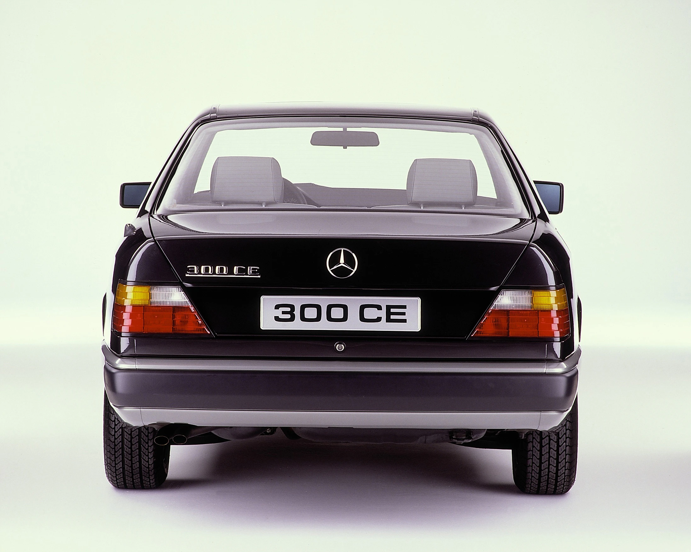 Rückansicht eines schwarzen Mercedes-Benz 300 CE mit sichtbarem Logo und Nummernschild auf hellem Hintergrund.