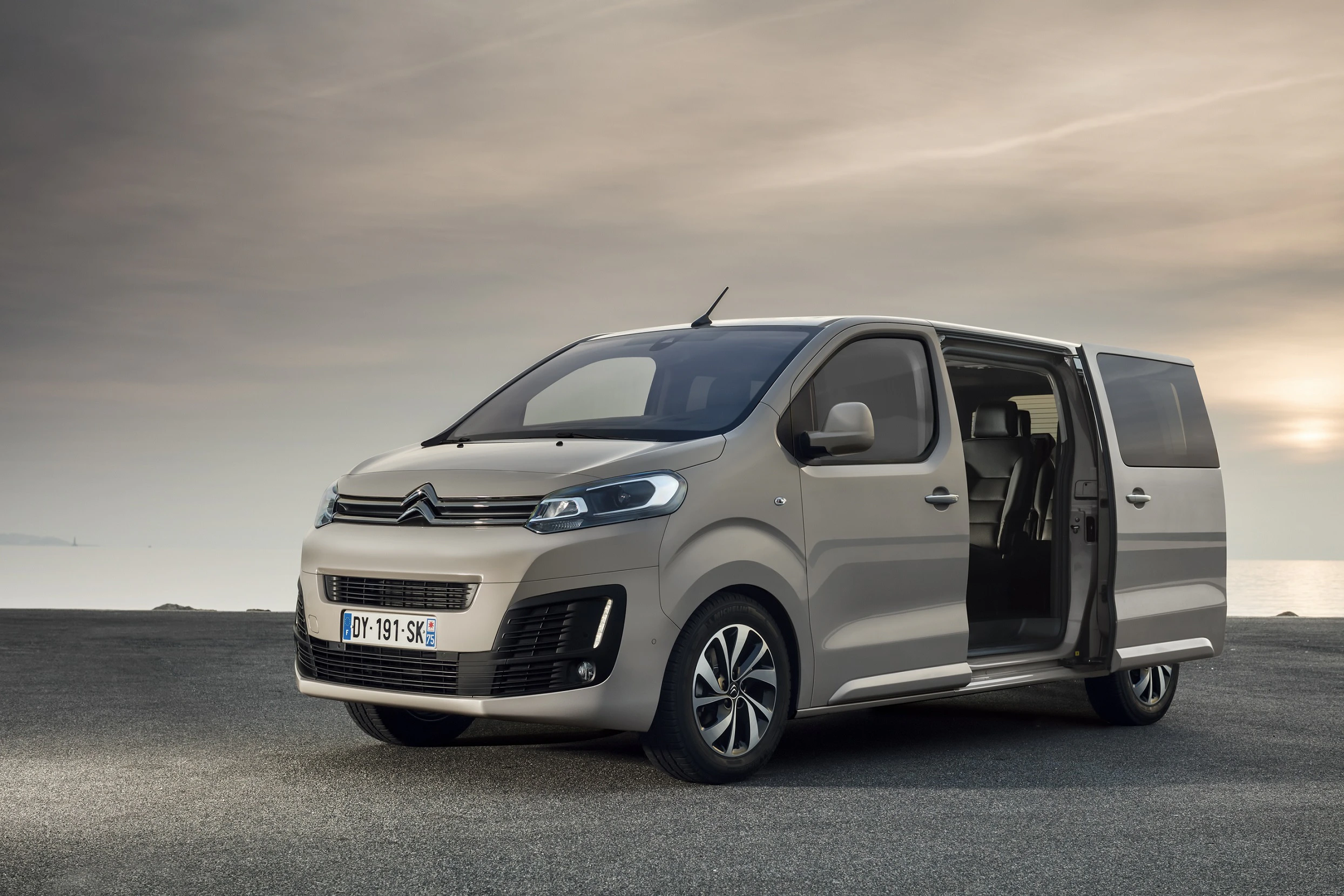 Beiger Citroën-Van steht auf einer Straße mit geöffneter Seitentür, im Hintergrund bewölkter Himmel.