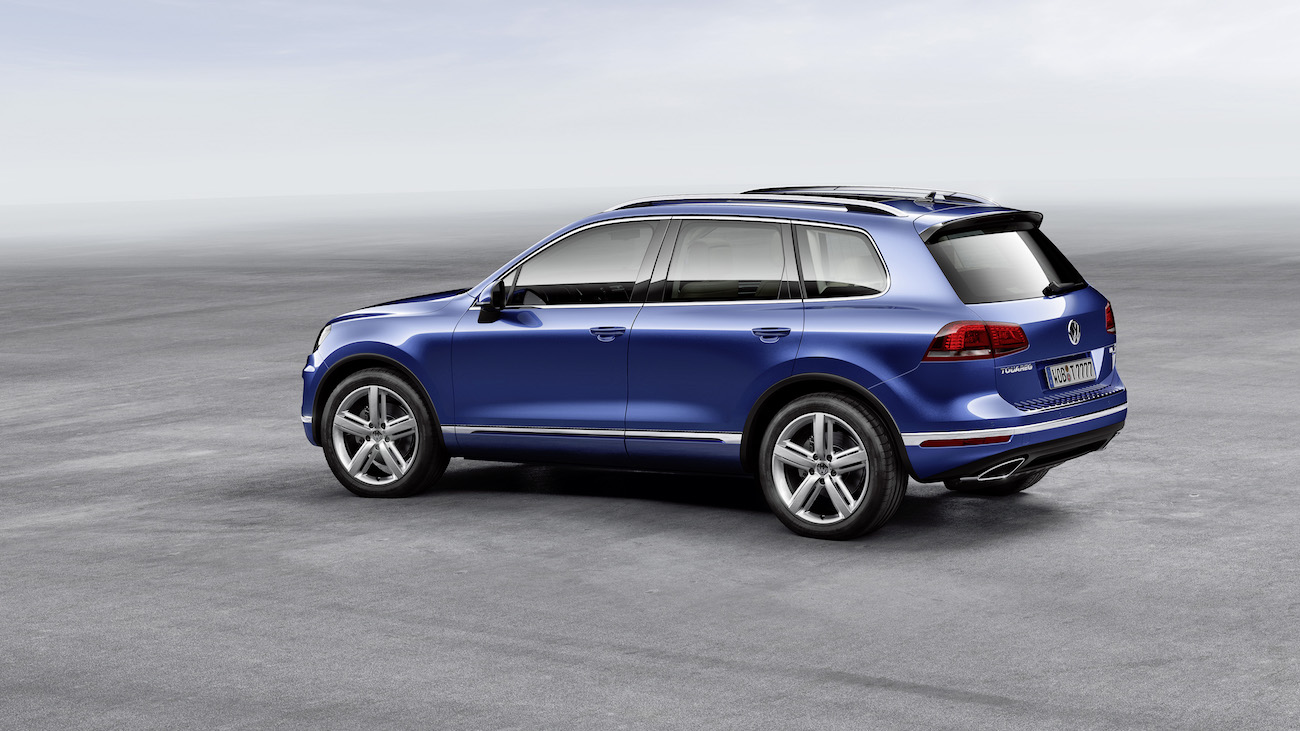 Blauer SUV steht auf einer asphaltierten Fläche vor einem hellen Himmel. Fahrzeug mit großen Rädern und sportlichem Design.