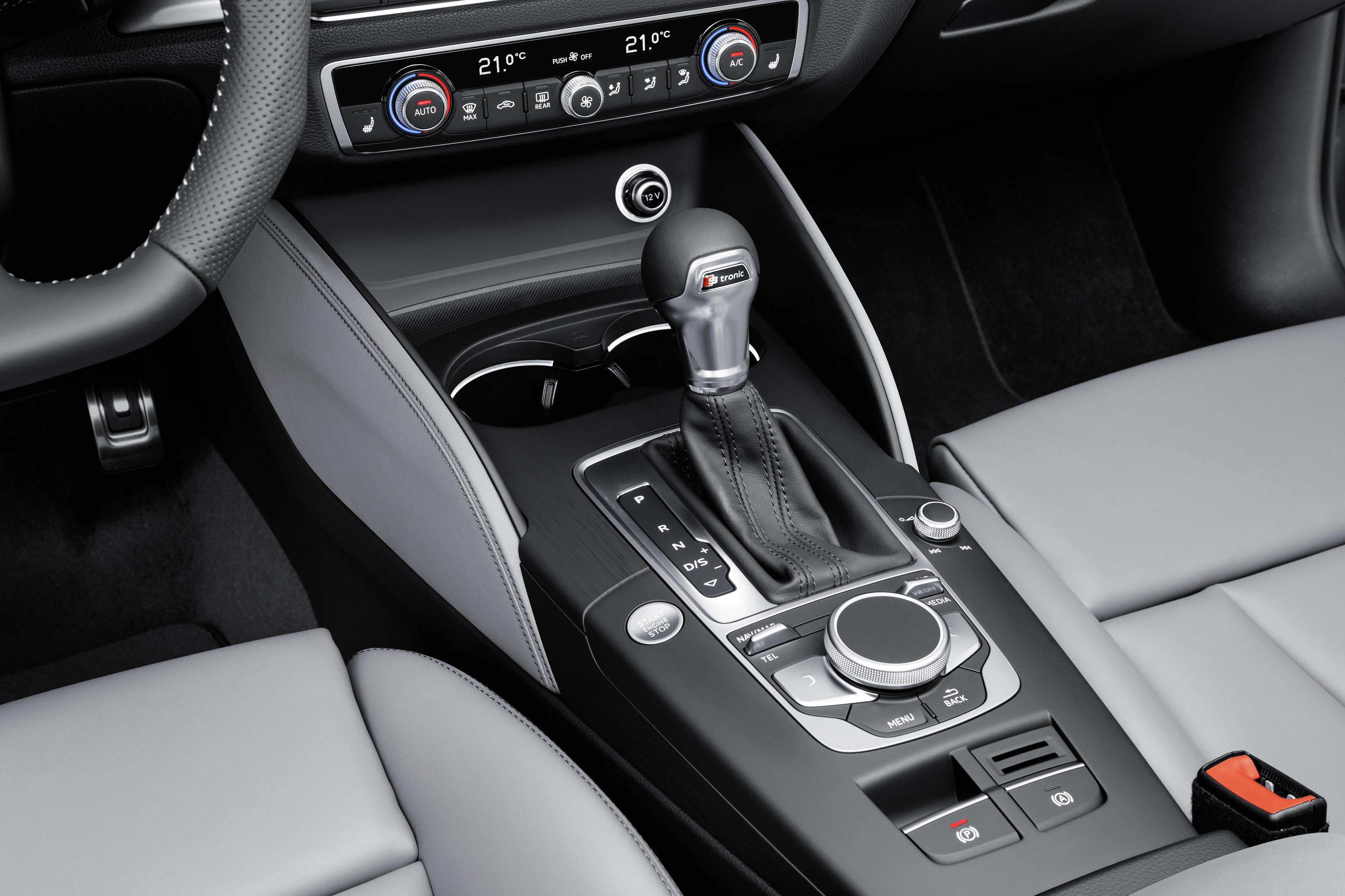 Nahaufnahme eines modernen Automatikgetriebes in einem Auto, umgeben von grauen Ledersitzen und einer Konsole mit verschiedenen Bedienelementen.