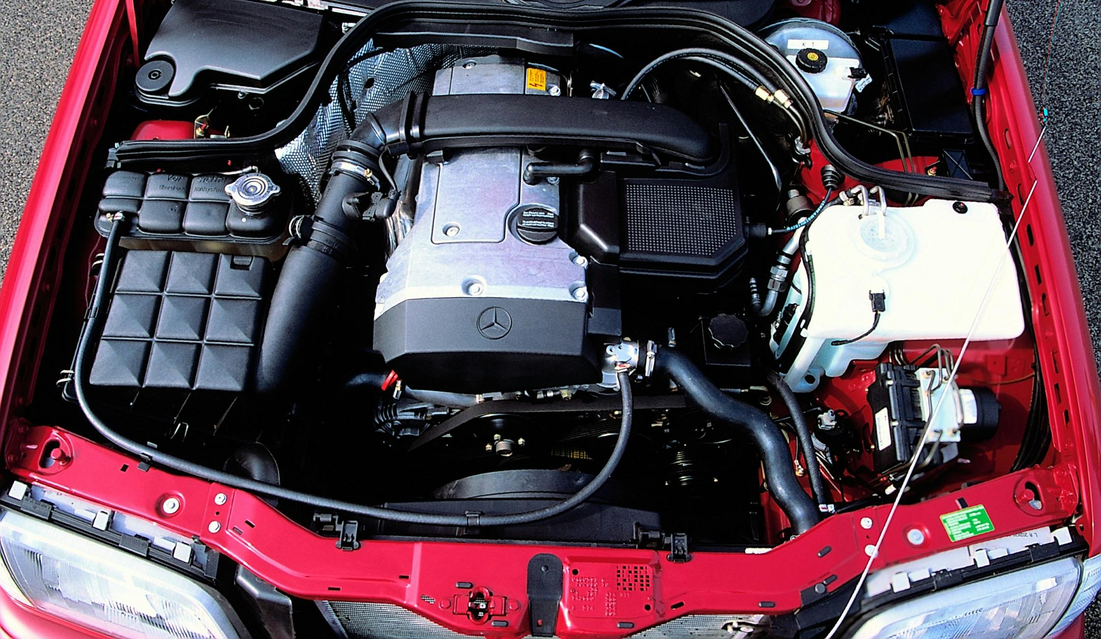 Roter Mercedes-Motorraum mit sichtbarem Motorblock, Kabeln und Schläuchen. Einige Bauteile sind mit dem Markenlogo versehen.