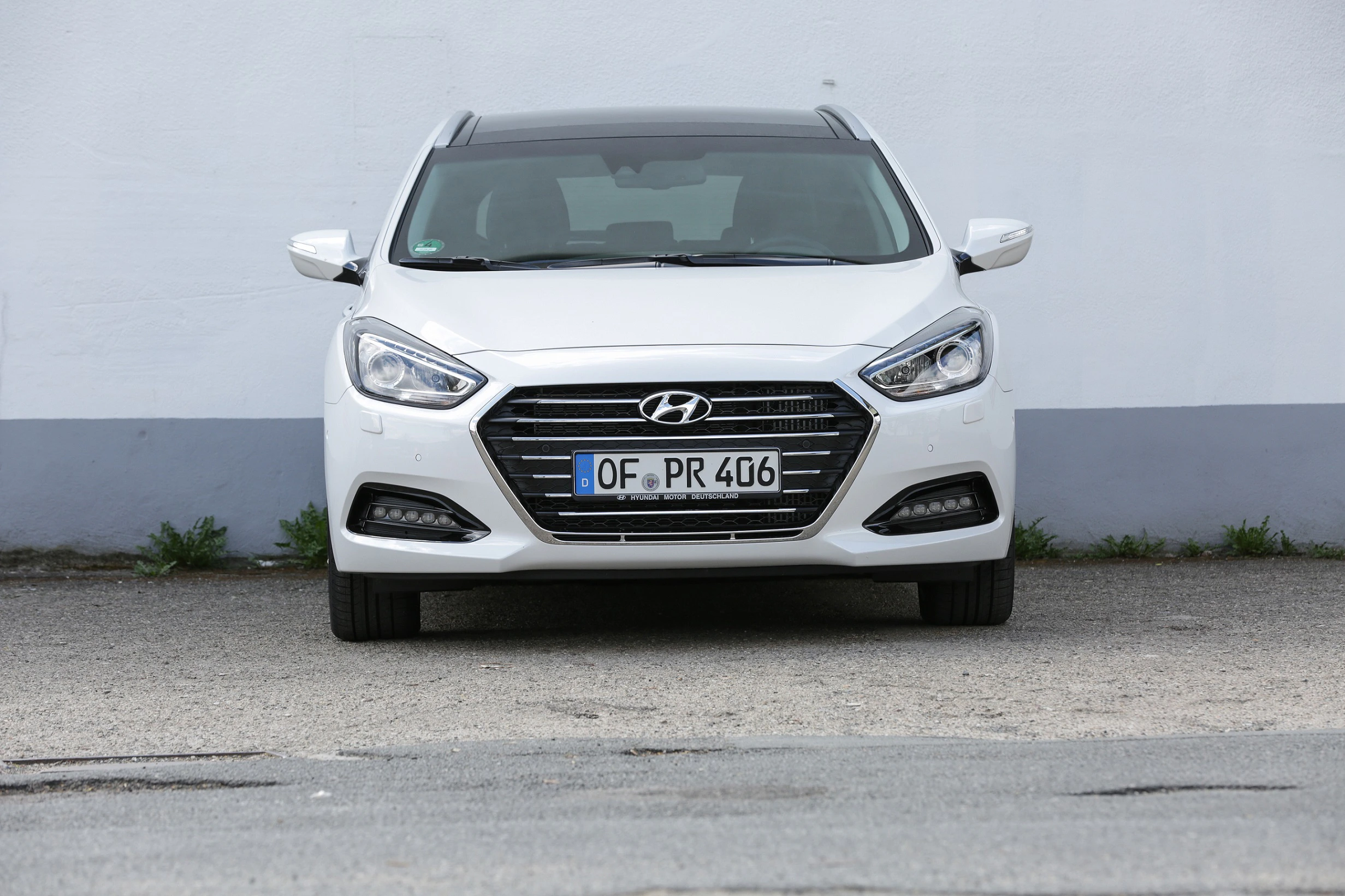 Weißer Hyundai i40 Kombi von vorne, auf einem asphaltierten Parkplatz vor einer grauen Wand geparkt.