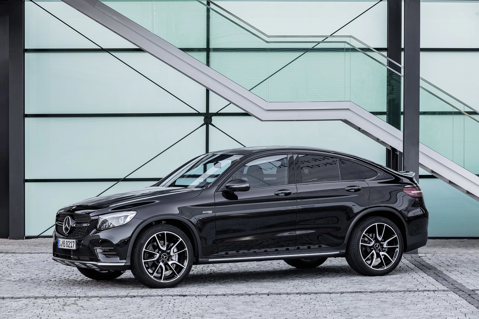Schwarzes Mercedes-Benz SUV vor moderner Glasfassade, seitliche Ansicht. Fahrzeug steht auf gepflasterter Fläche, im Hintergrund Treppe.