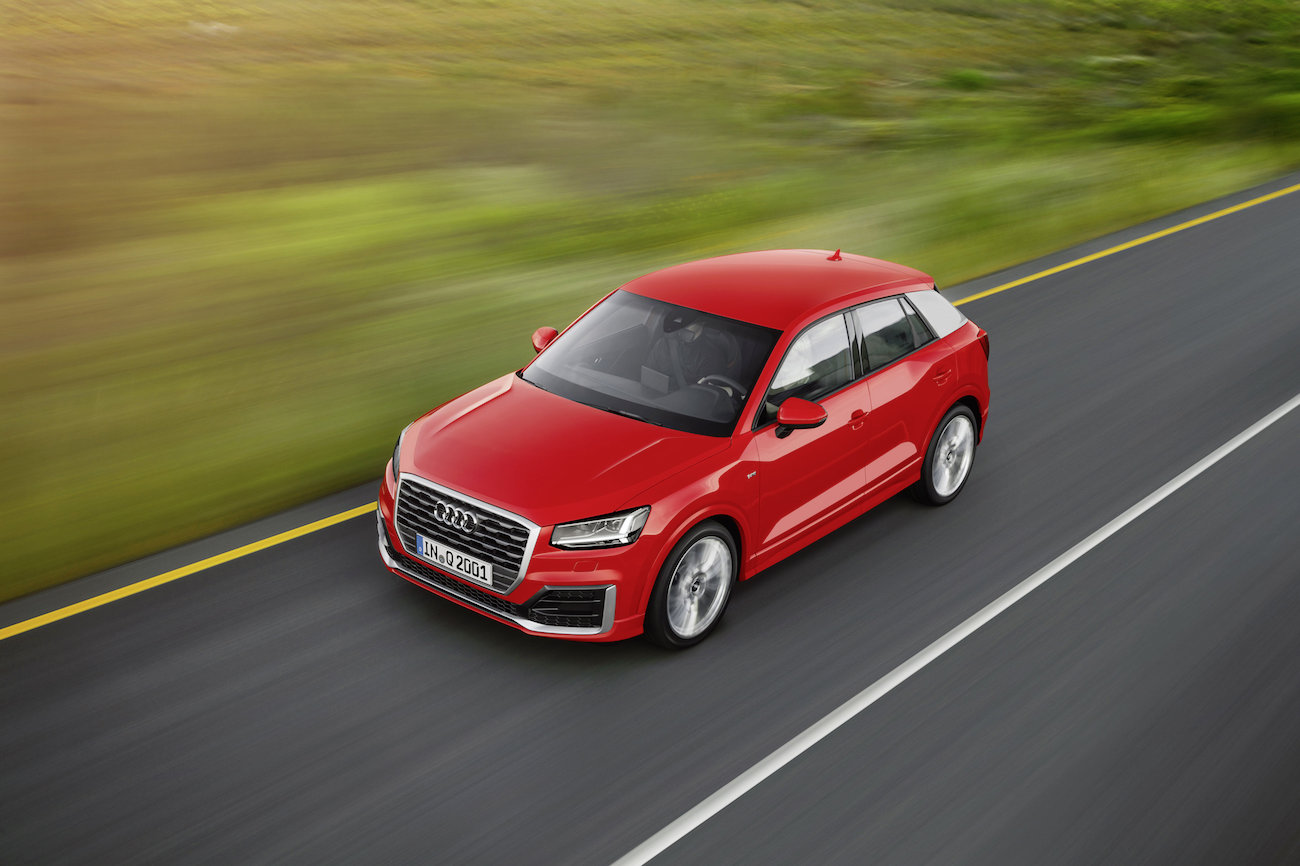 Roter SUV fährt auf einer Landstraße entlang grüner Wiesen in schneller Bewegung von oben aufgenommen.