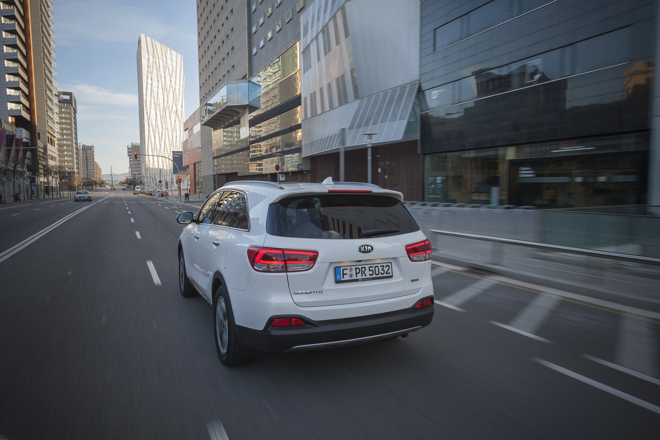 Ein weißer SUV fährt durch eine moderne Stadt mit hohen Glasgebäuden und leerer Straße.