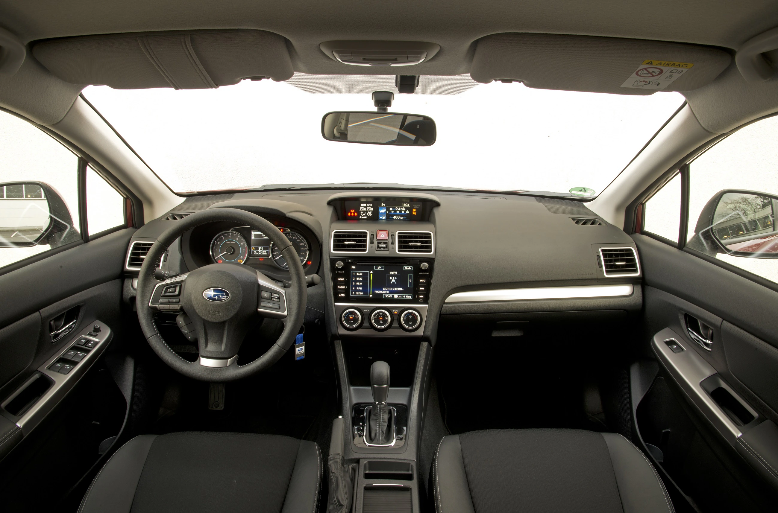 Innenraum eines Autos mit Lenkrad links, digitalem Display, zentraler Konsole mit Schaltern und Belüftungsdüsen, schwarzes Interieur.