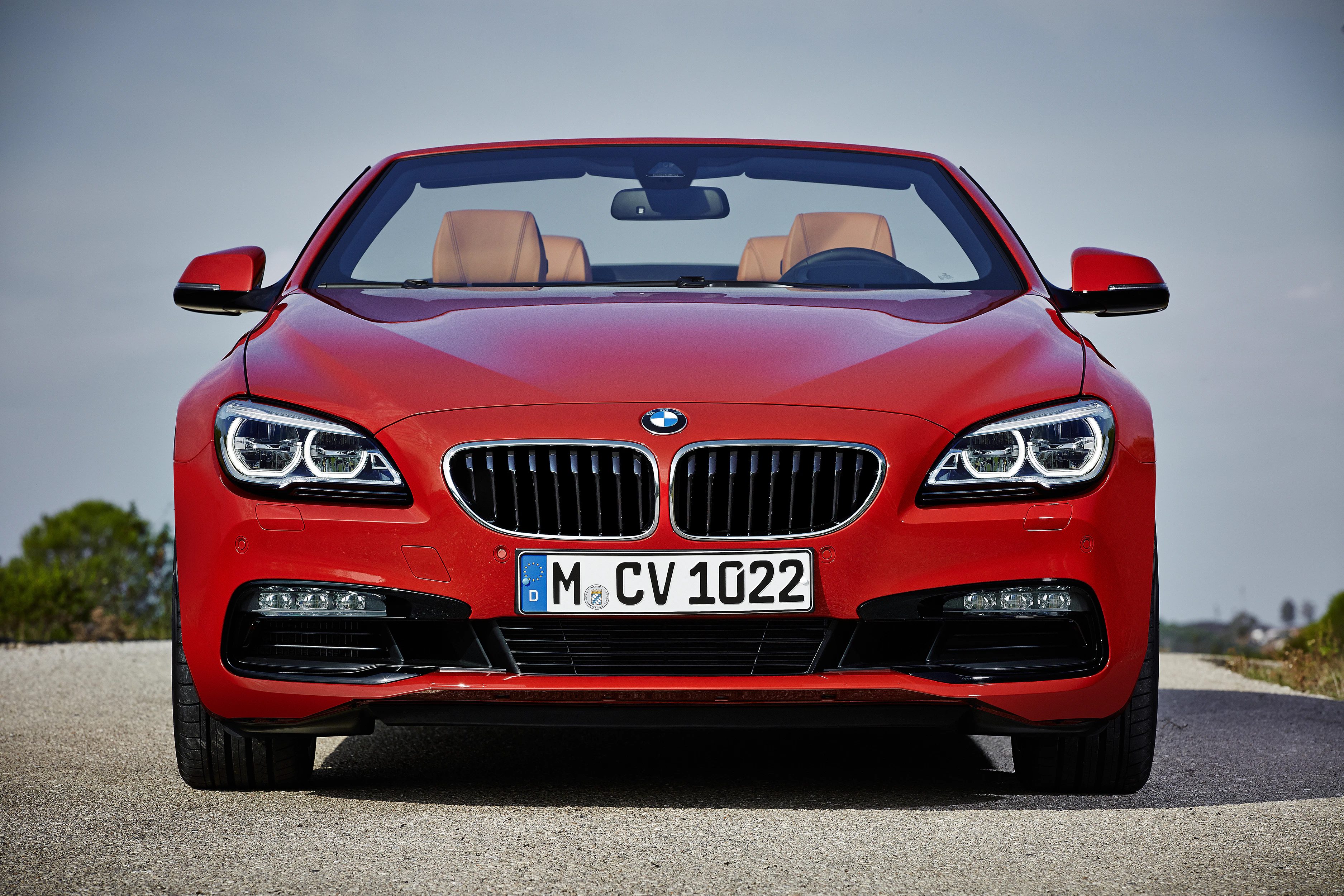 Rotes BMW-Cabriolet auf einer Straße, mit geöffnetem Verdeck und braunen Ledersitzen.