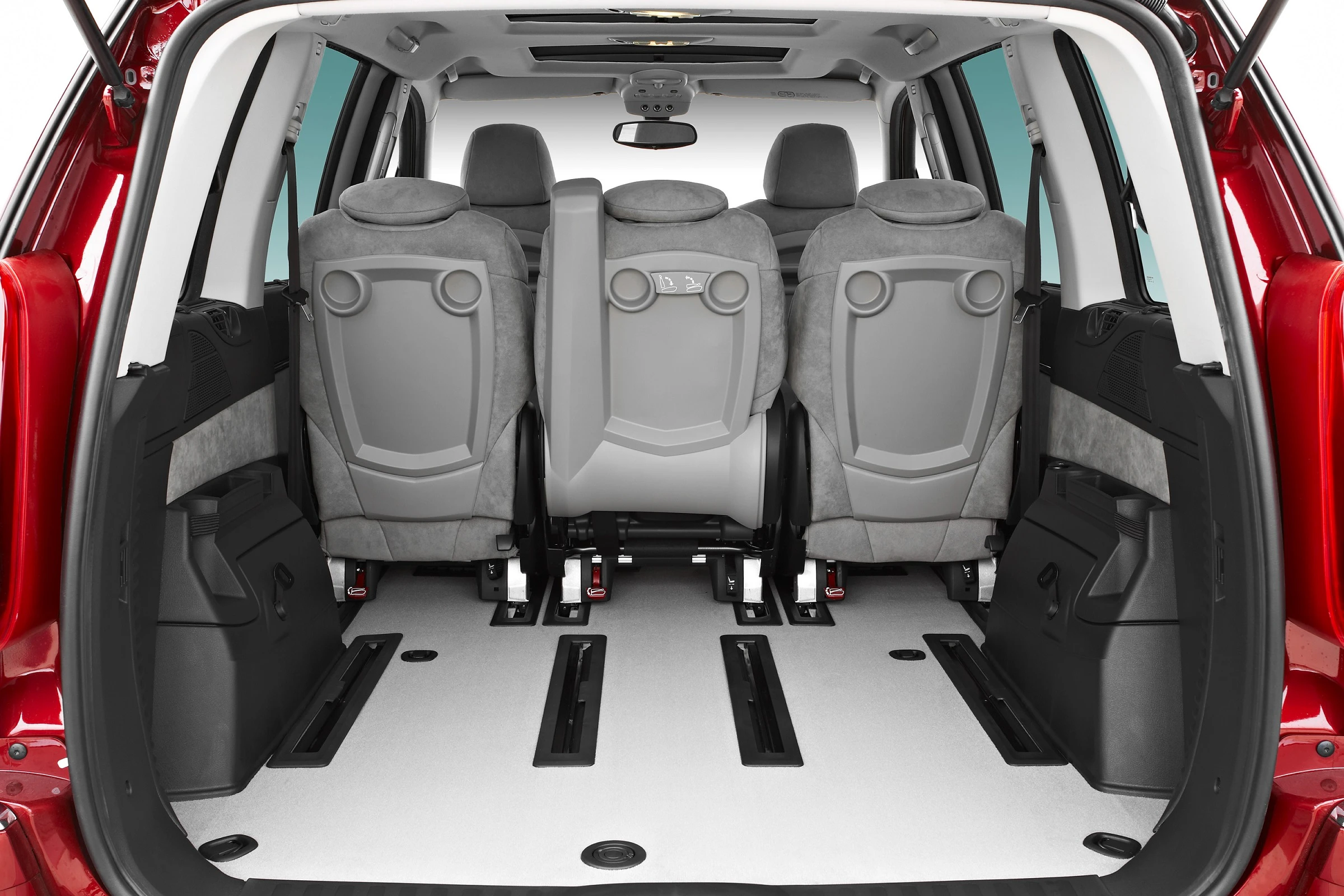 Innenansicht eines Minivans von hinten, zeigt drei Sitzreihen und einen großzügigen Laderaum. Sitze in Grau, mit roter Außenfarbe des Autos.