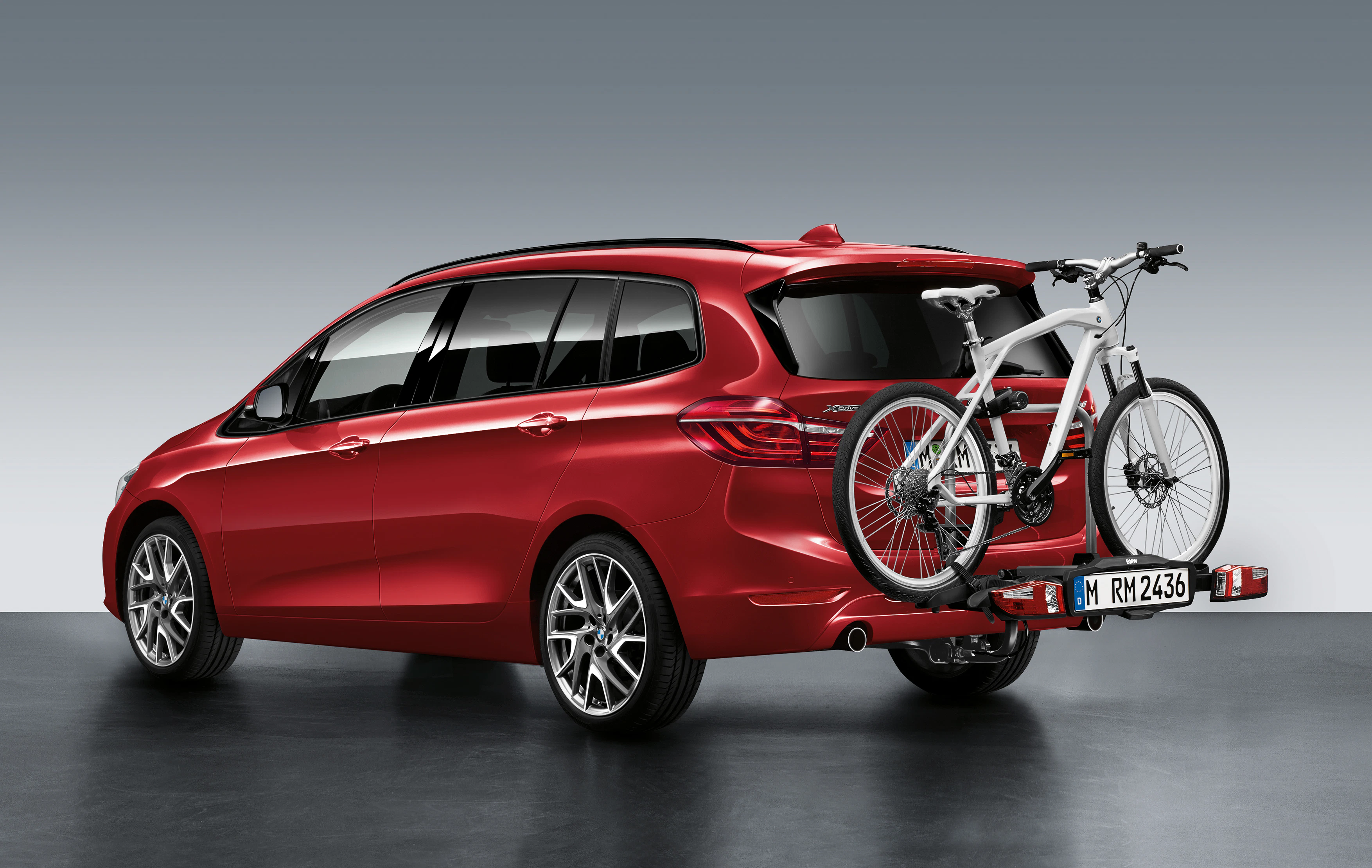 Rotes Auto mit Fahrradträger, der ein weißes Fahrrad transportiert. Auto geparkt, Rückansicht sichtbar auf grauem Hintergrund.