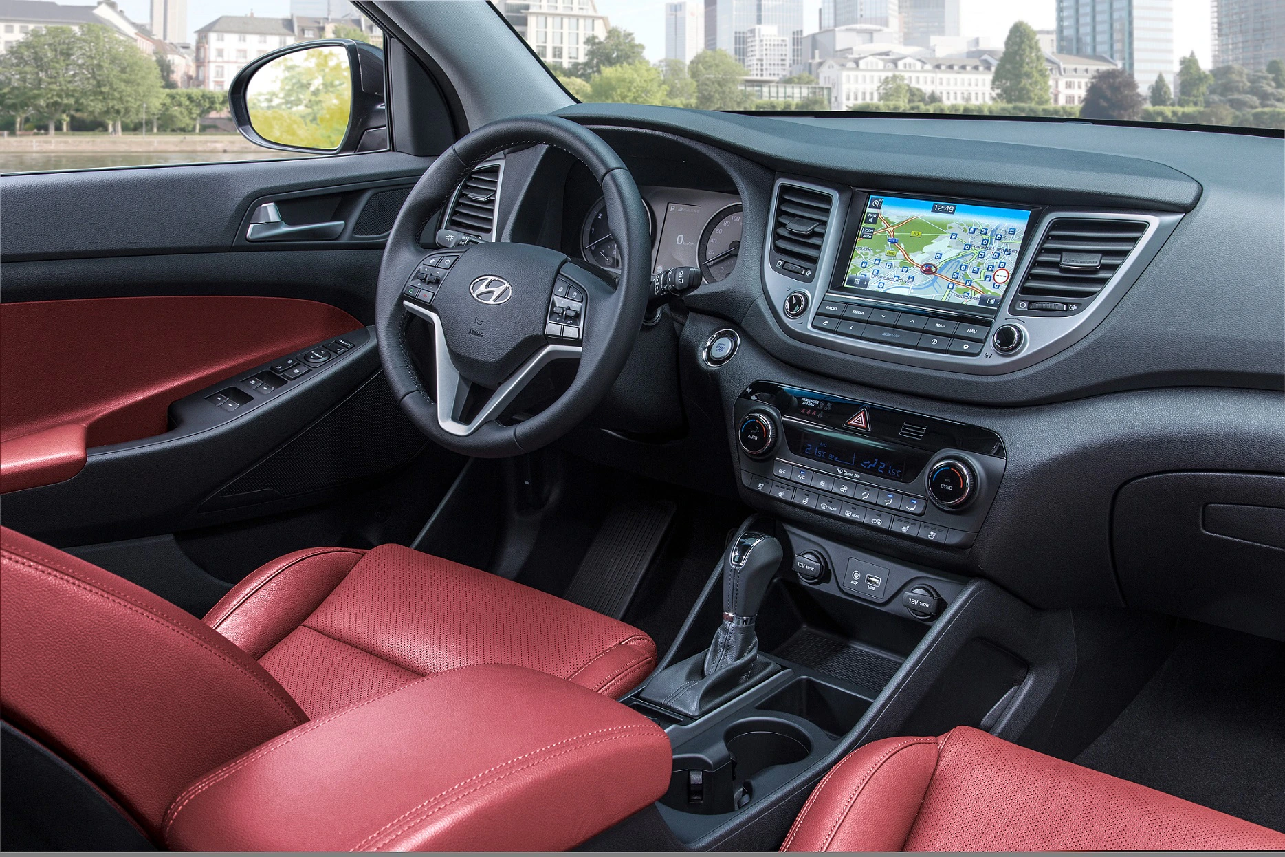 Innenraum eines Autos mit rotem Ledersitz, Lenkrad, Schalthebel und integriertem Navigationssystem auf dem Bildschirm.