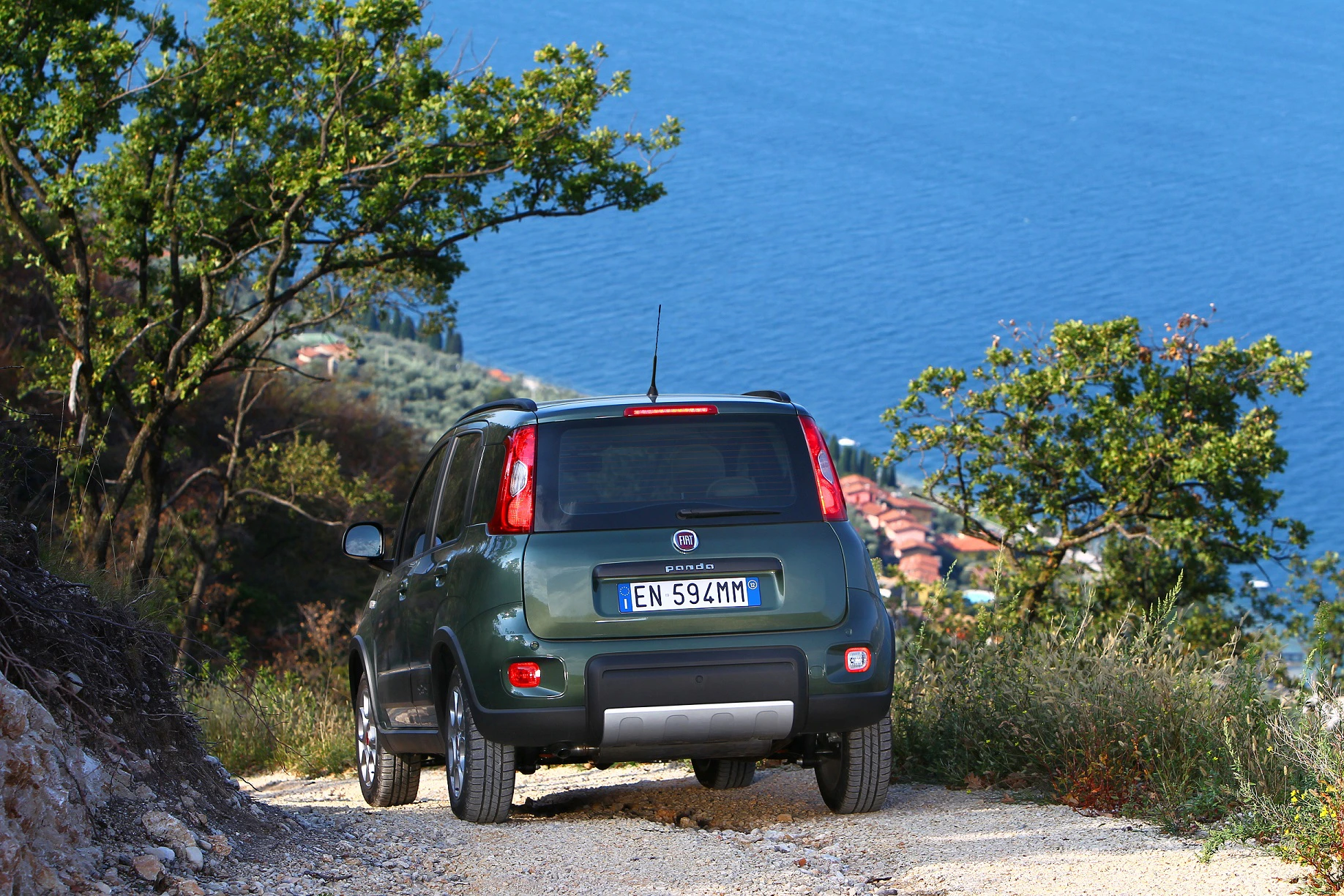 Ein grüner SUV fährt einen unbefestigten Weg entlang. Im Hintergrund sind das Meer und Bäume zu sehen.
