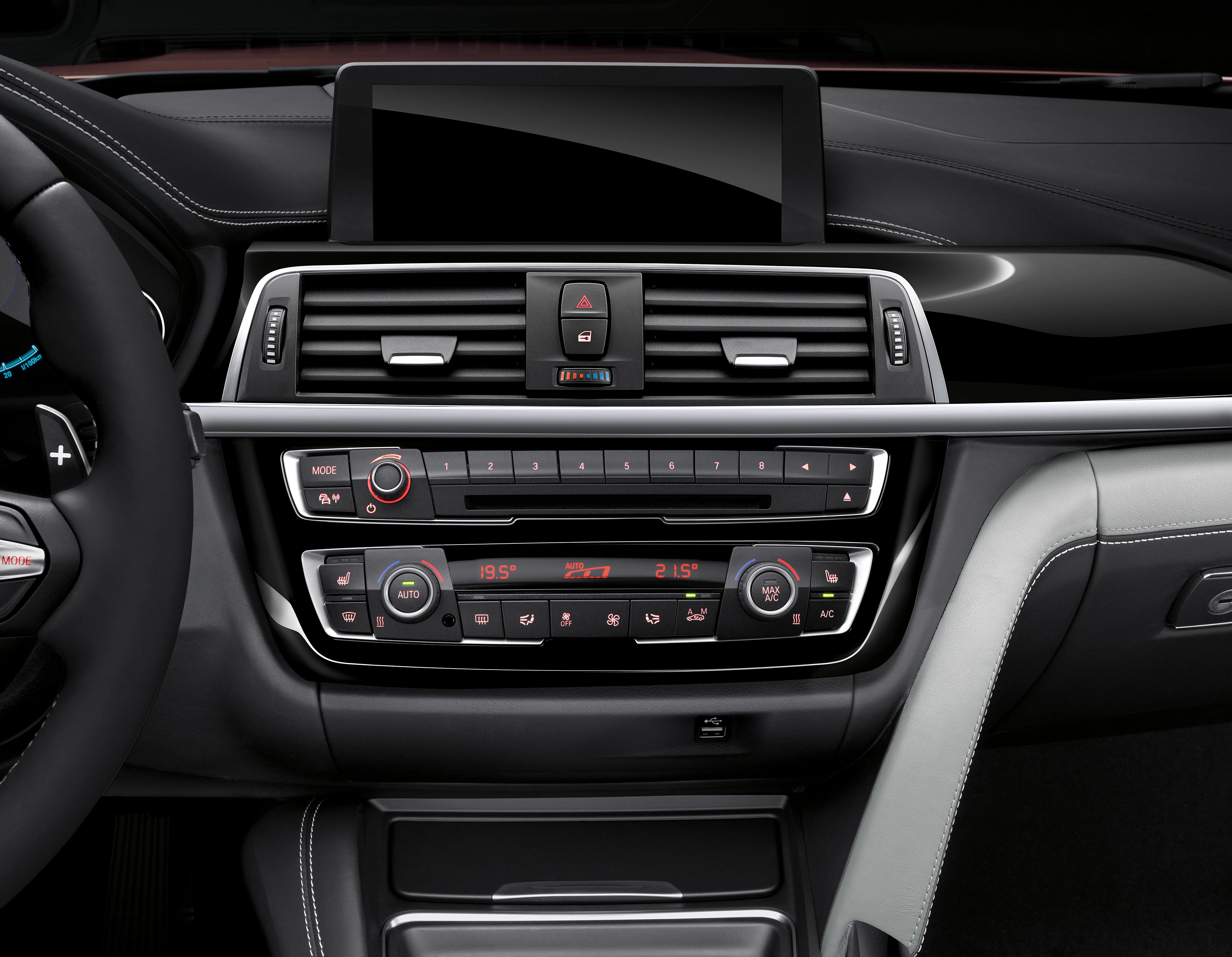 Mittelkonsole eines Autos mit Bildschirm, Lüftungsschlitzen und Bedienelementen für Klimaanlage und Audio, in schwarzem Interieur.