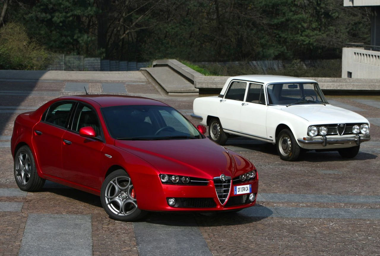 Roter und weißer Alfa Romeo auf gepflastertem Platz. Der rote Wagen ist moderner, der weiße ist ein klassisches Modell mit eckigen Formen.