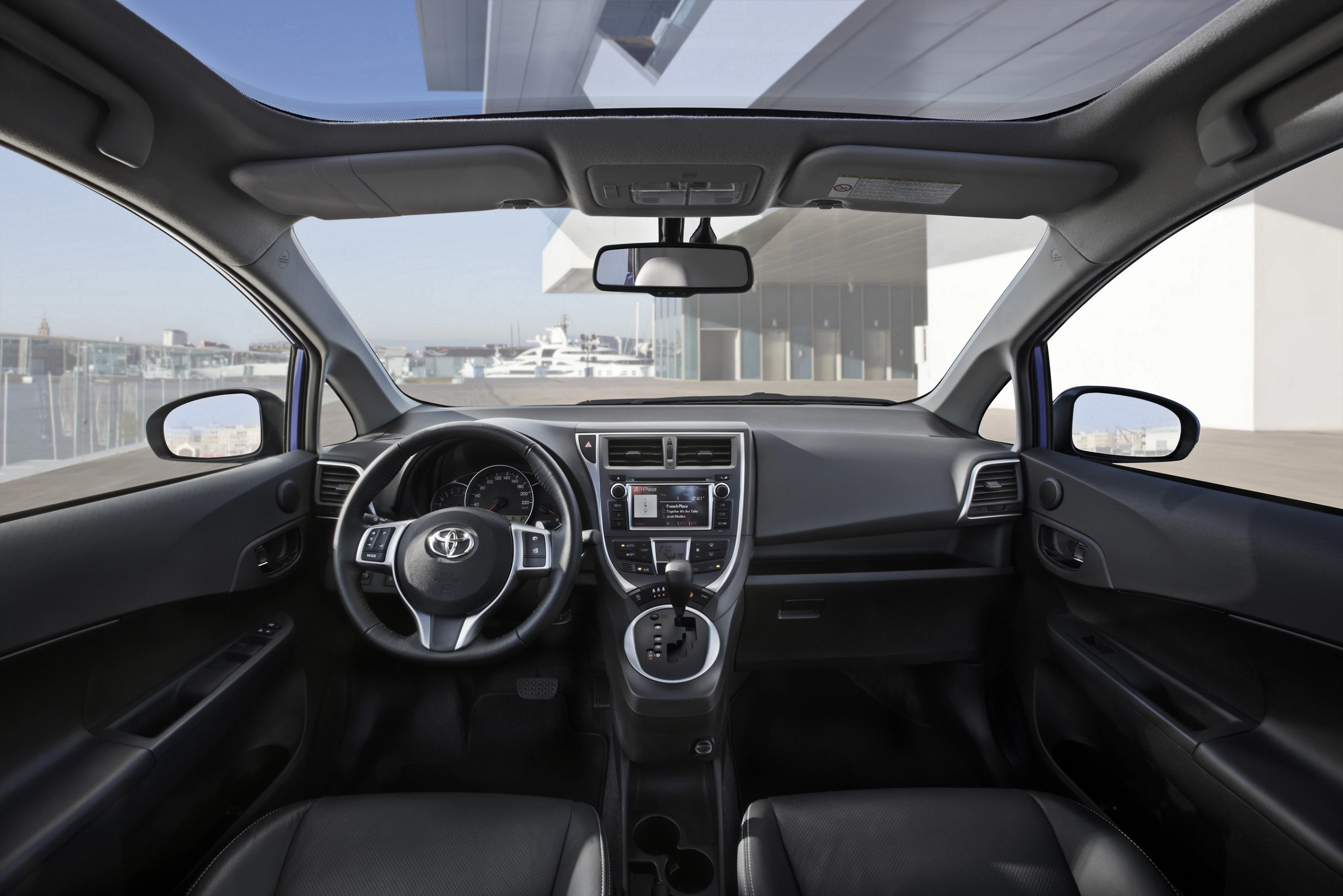 Innenansicht eines Autos mit einem modernen Armaturenbrett, Lenkrad mit Toyota-Logo und großem Bildschirm in der Mittelkonsole.