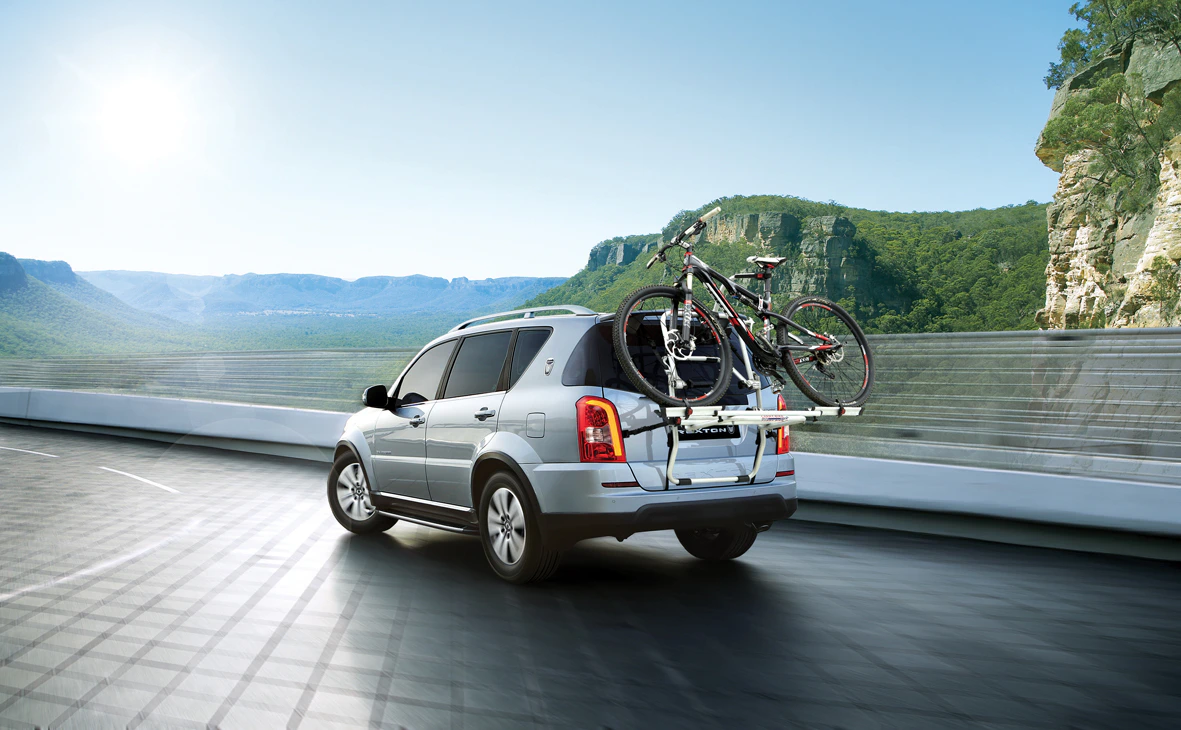 Silbernes SUV fährt auf einer Straße durch eine bergige Landschaft. Zwei Fahrräder sind auf einem Heckträger befestigt.