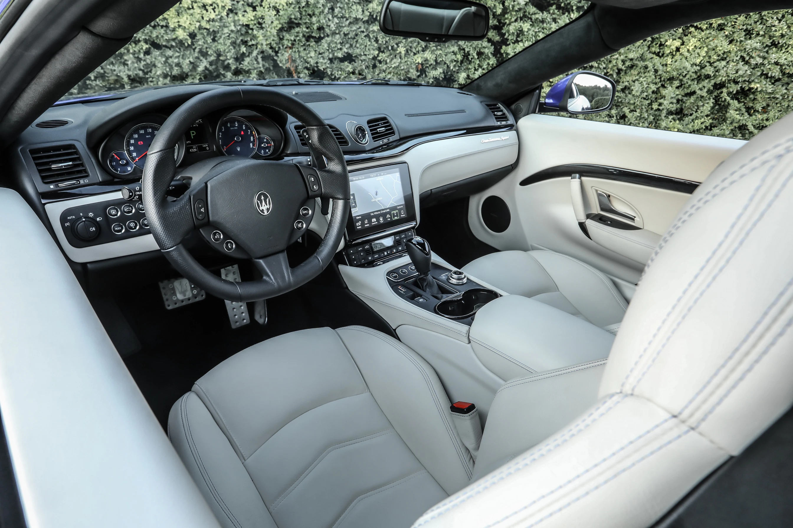 Innenraum eines Luxusautos mit hellgrauen Ledersitzen, modernem Armaturenbrett, Multifunktionslenkrad und eingebautem Navigationssystem.