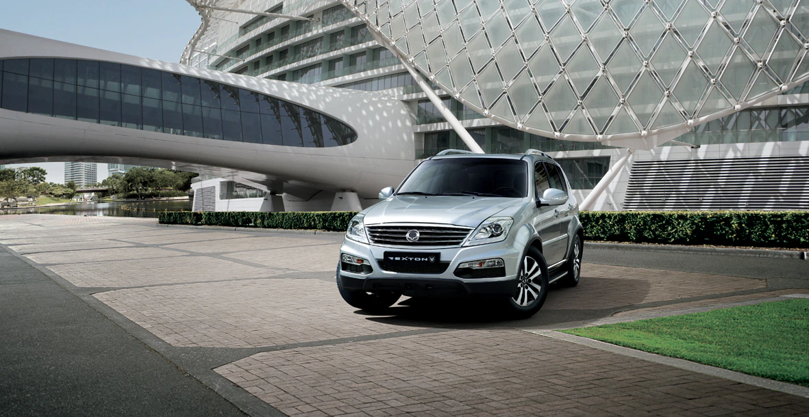 Silberner SUV geparkt vor einem modernen Gebäude mit Glasfassade und geschwungenem Design, bei sonnigem Wetter.