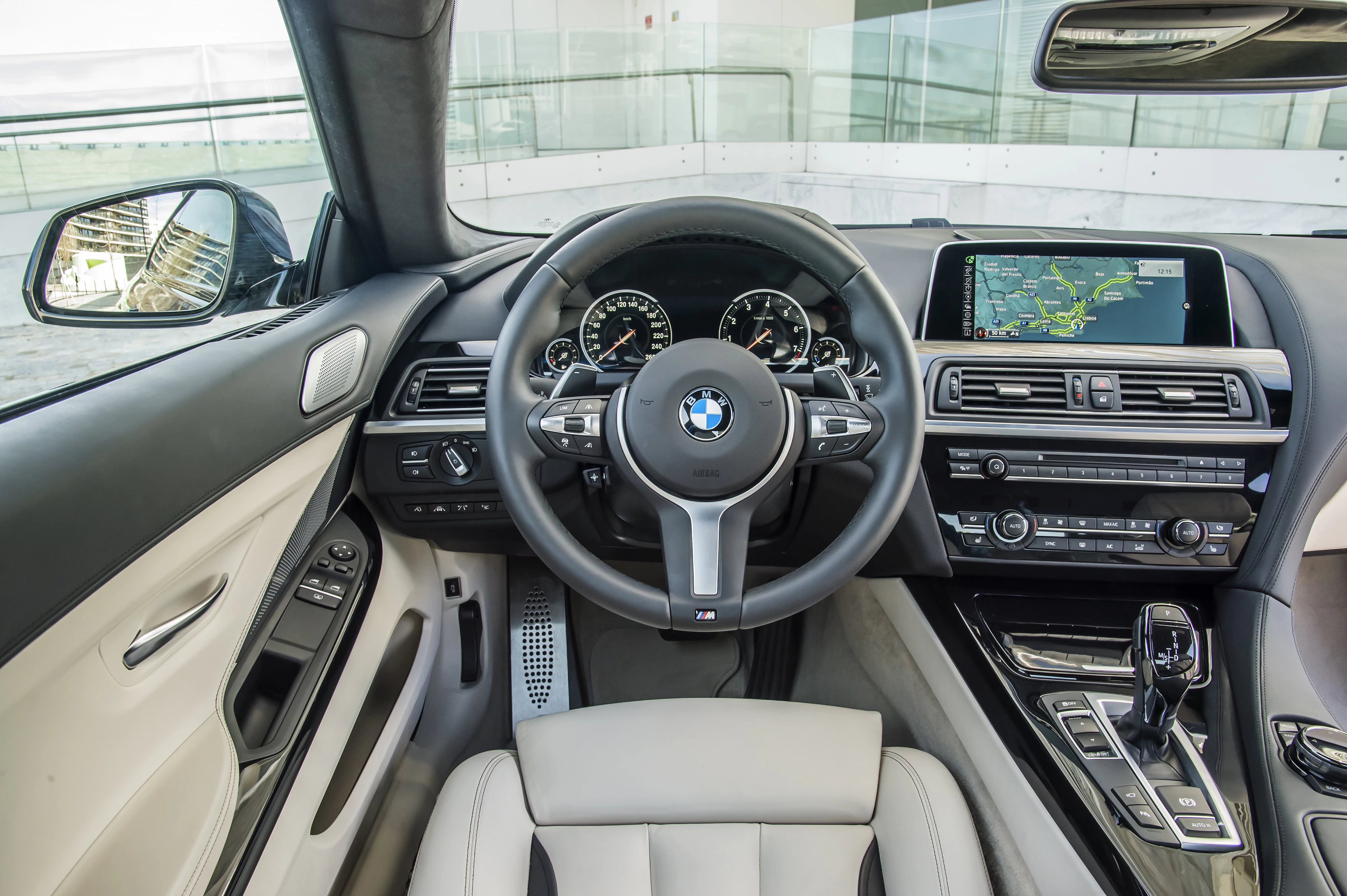 BMW-Innenraum mit modernen Armaturen, Lenkrad mit Logos, digitale Anzeige und Navigationssystem. Helle Ledersitze.
