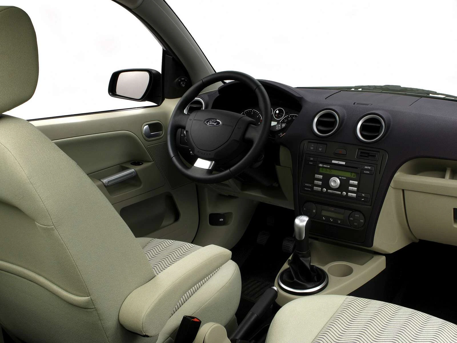 Innenraum eines Autos mit grauen Sitzen, Lenkrad, Schalthebel und Armaturenbrett mit integriertem Radio und Lüftungsschlitzen.