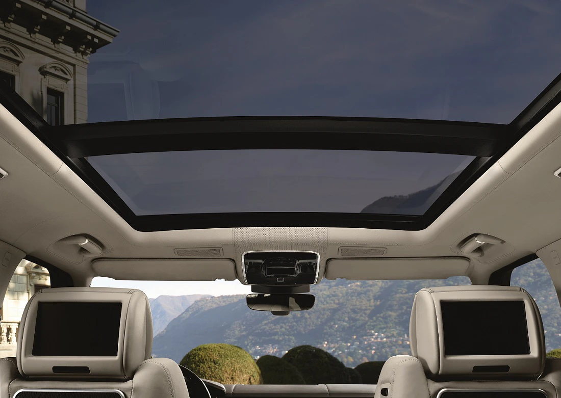 Innenraum eines Autos mit Panoramadach. Im Hintergrund sind Berge und ein Himmel durch das Dachfenster sichtbar. Zwei Kopfstützen vorne.
