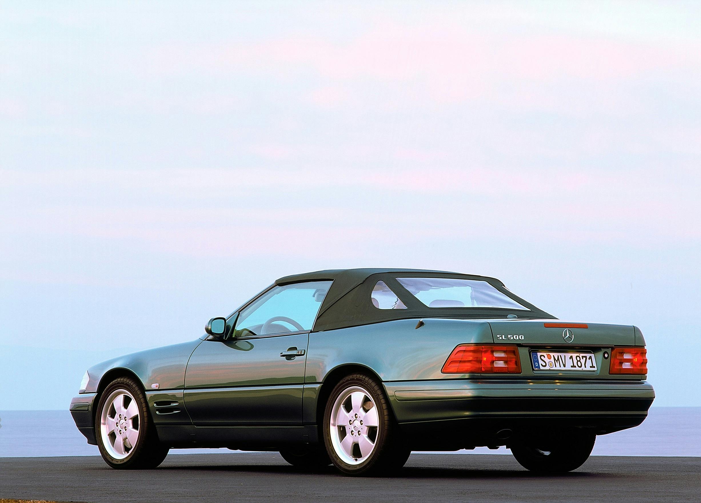 Grüner Mercedes-Benz Cabrio, Modell SL 500, auf einer Straße vor einem pastellfarbenen Himmel geparkt, Rückansicht.
