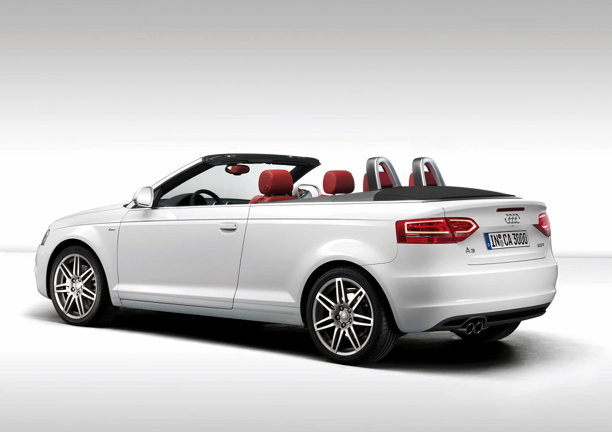 Weißes Audi Cabrio mit schwarzem Verdeck, roten Sitzen und silbernen Felgen, seitlich von hinten gezeigt.