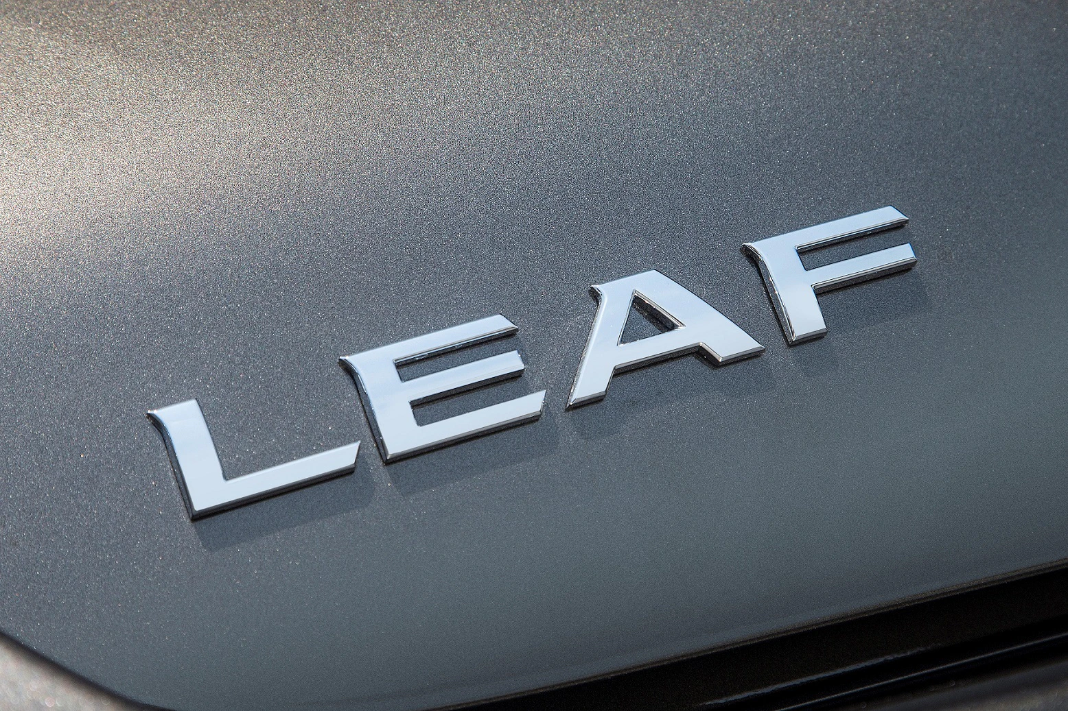 Nahaufnahme des Wortes "LEAF" in glänzenden Silberbuchstaben auf einem grauen Autolack.