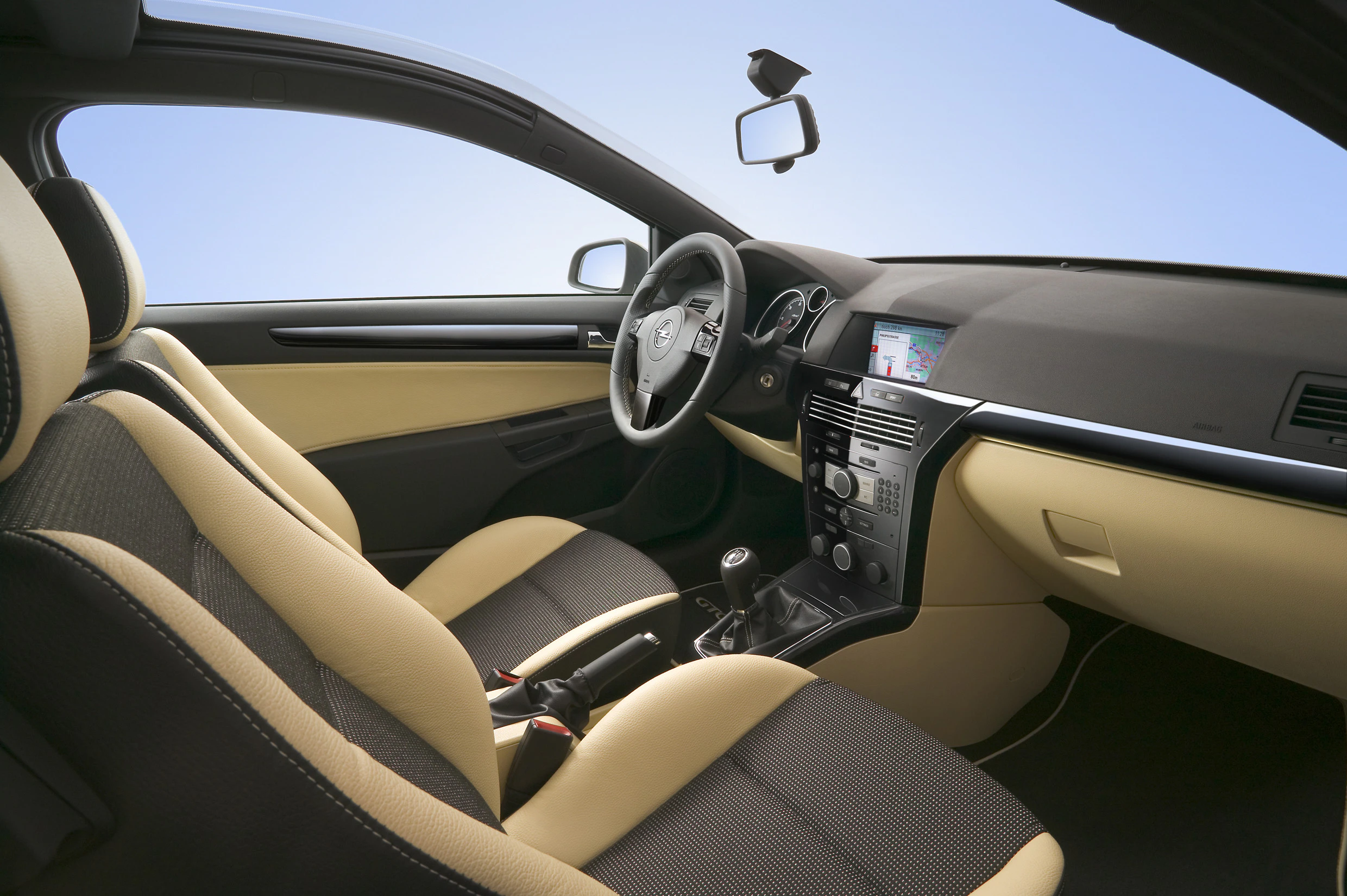 Innenraum eines modernen Autos mit beigefarbenen Ledersitzen, schwarzem Armaturenbrett, manuellem Schaltgetriebe und integriertem Navigationssystem.