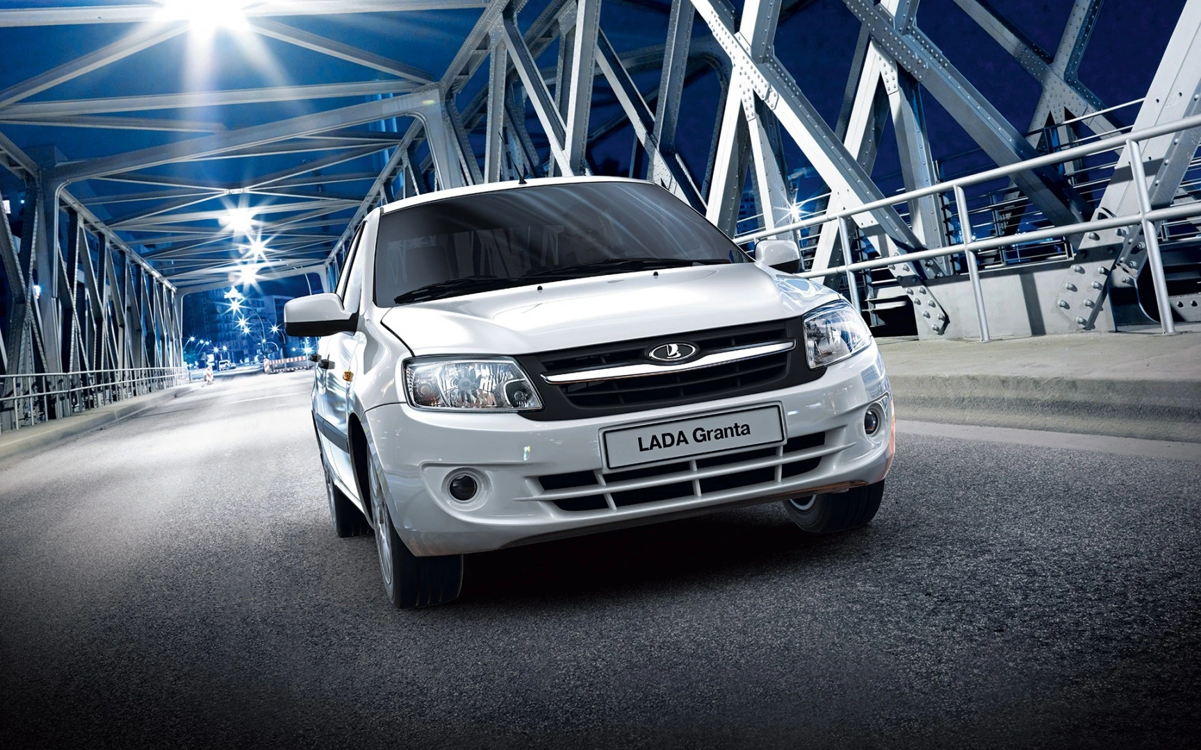 Weißer Lada Granta fährt nachts über eine beleuchtete Brücke mit Metallstruktur.