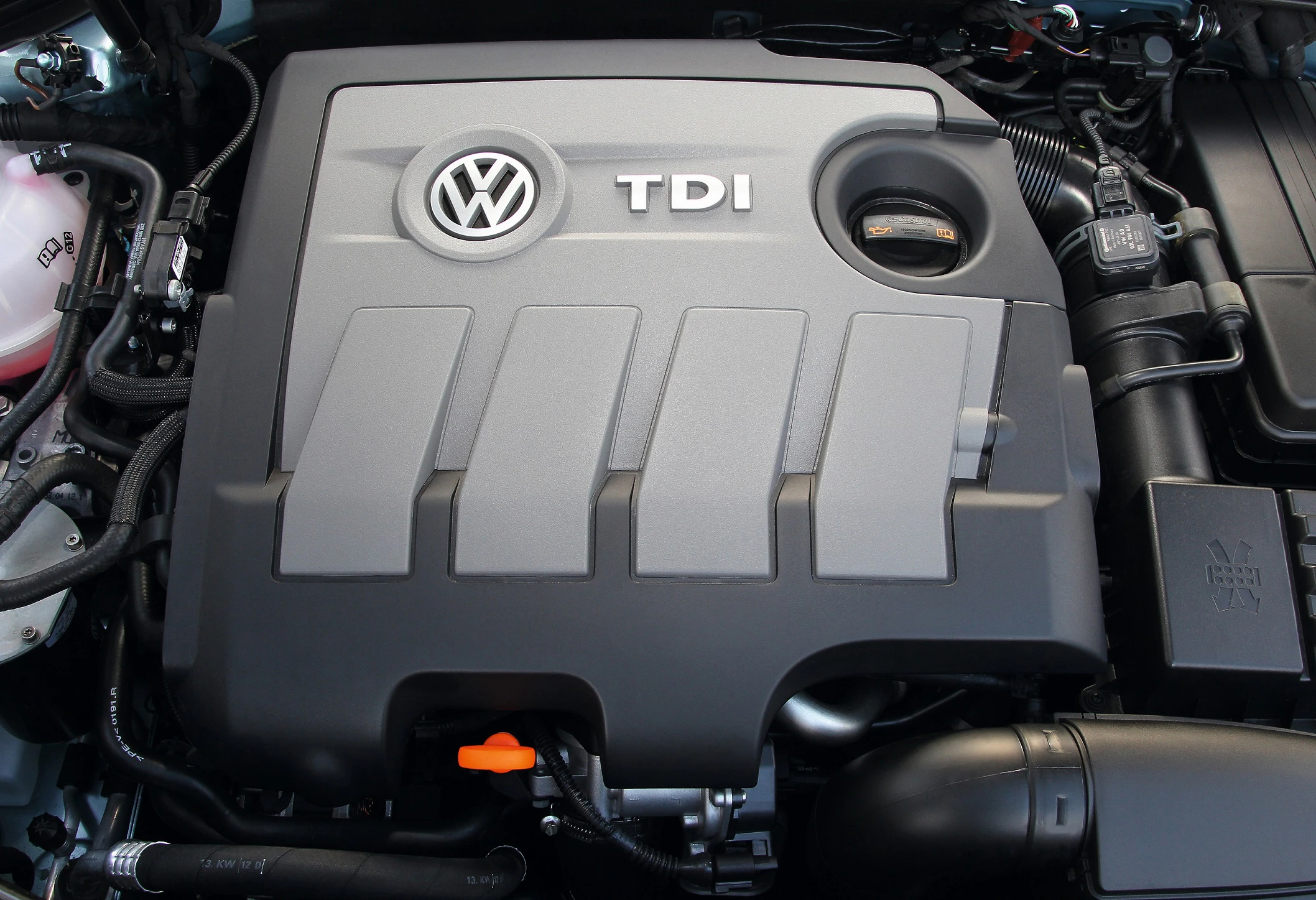 VW TDI-Motor mit einem grauen Abdeckungsmodul, sichtbarem Öldeckel und umliegenden Motorbauteilen im Fahrzeug.