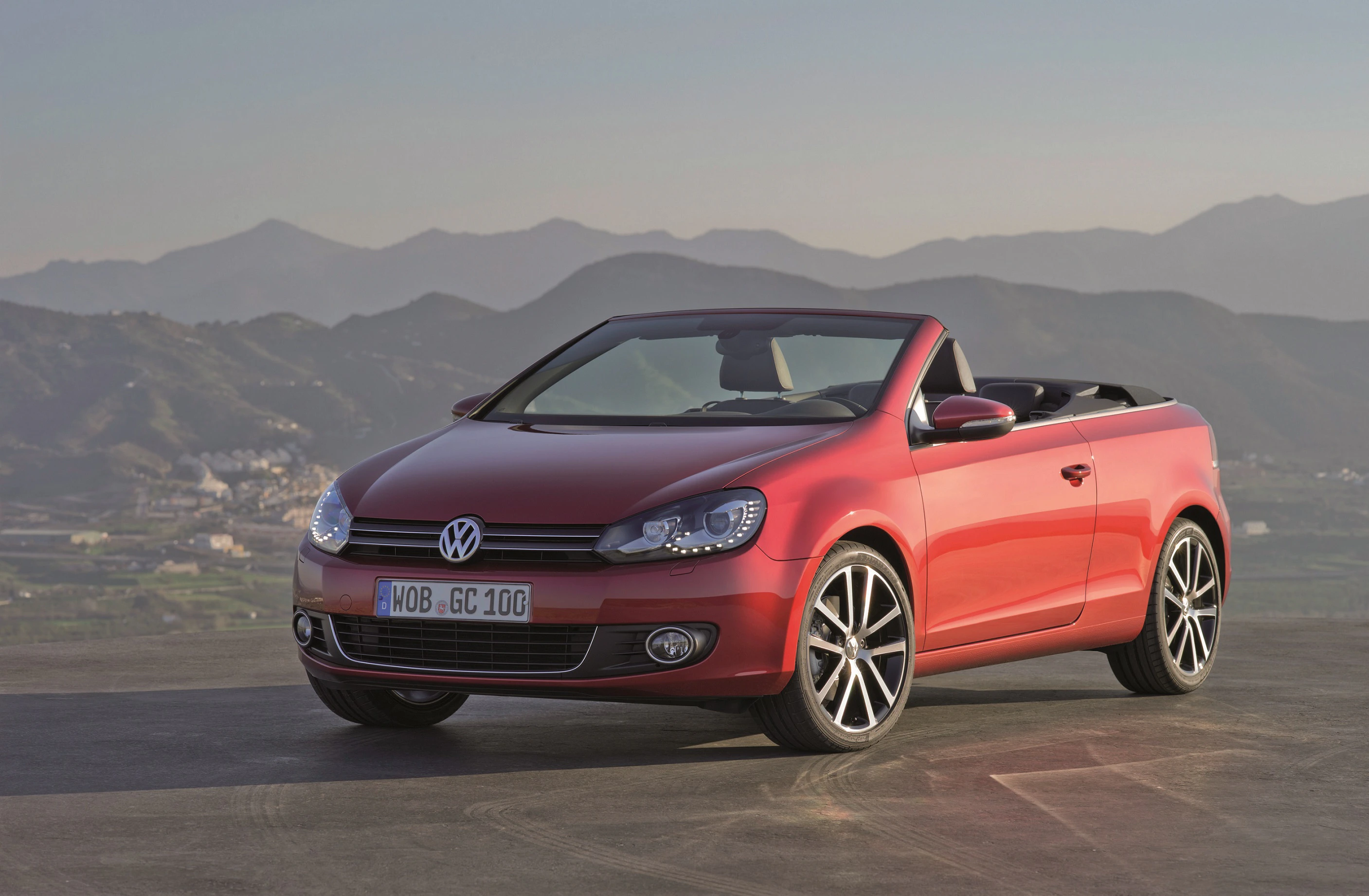 Rotes Volkswagen Cabrio auf einem Hügel, im Hintergrund Berge bei Sonnenuntergang.