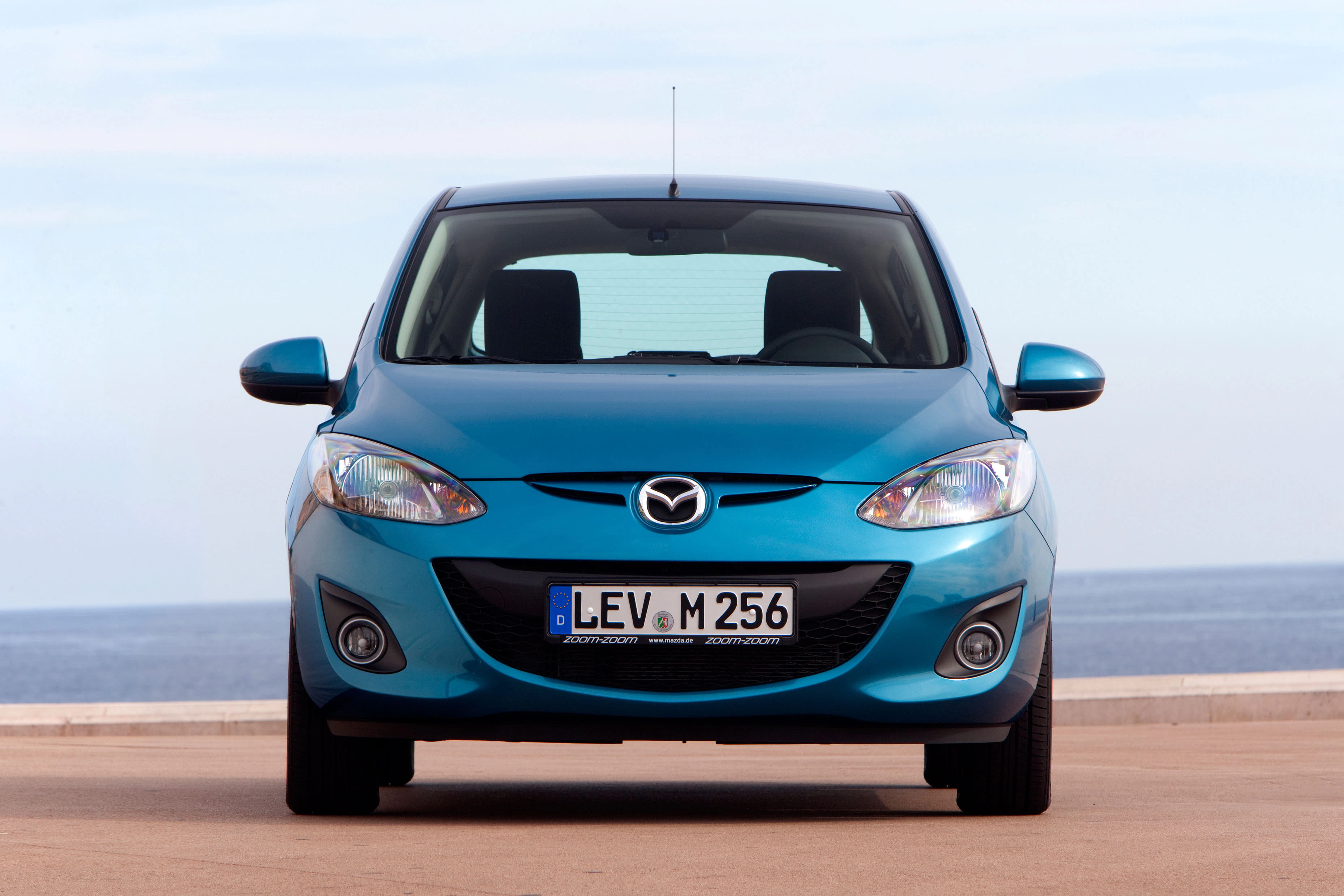 Blauer Mazda mit Kennzeichen LEV M 256, geparkt auf einer Küstenstraße mit Meereshorizont im Hintergrund.