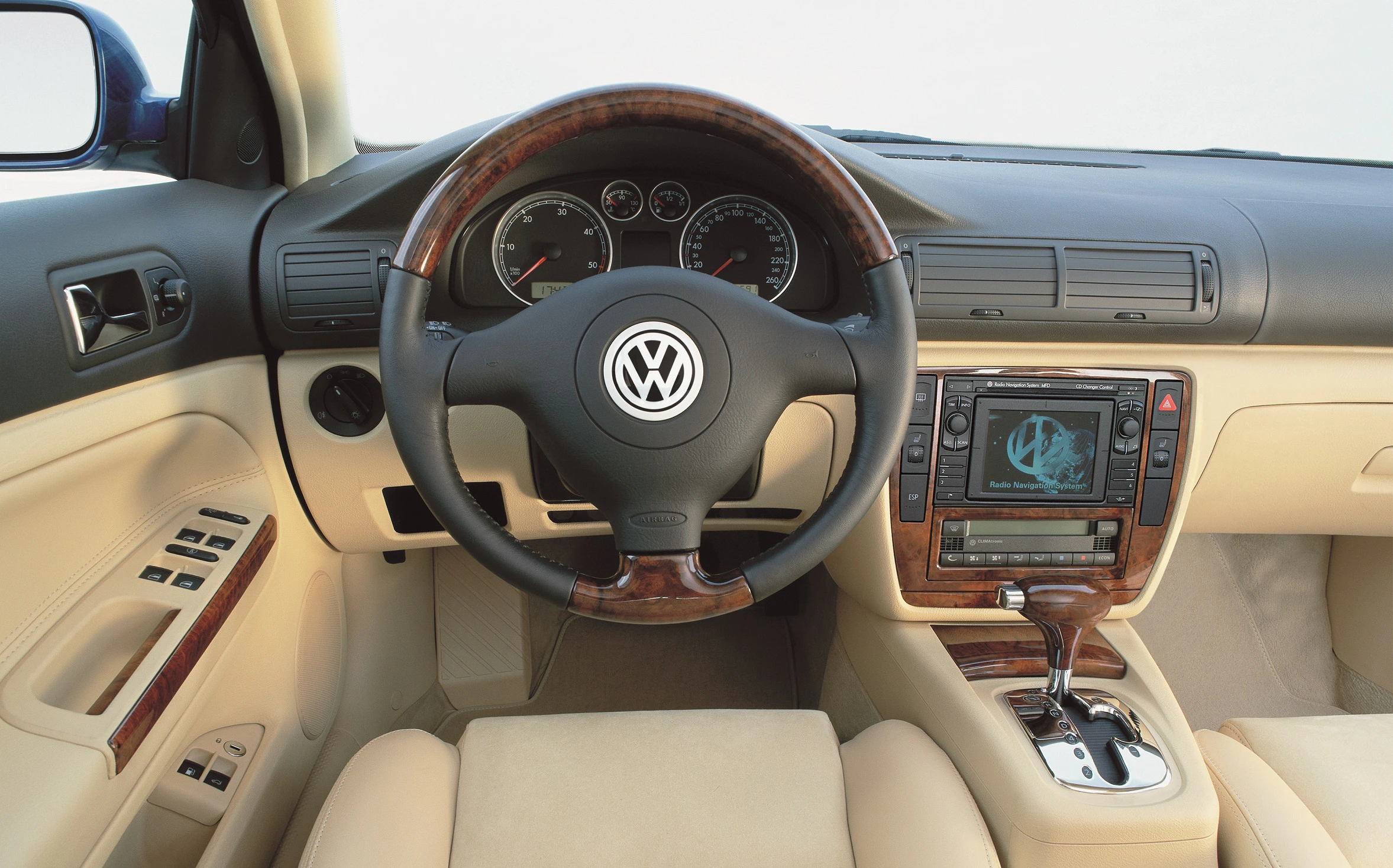 Innenraum eines Volkswagen mit Holzverkleidung, Lederlenkrad, Navigationssystem und Automatikgetriebe. Beige Ledersitze.